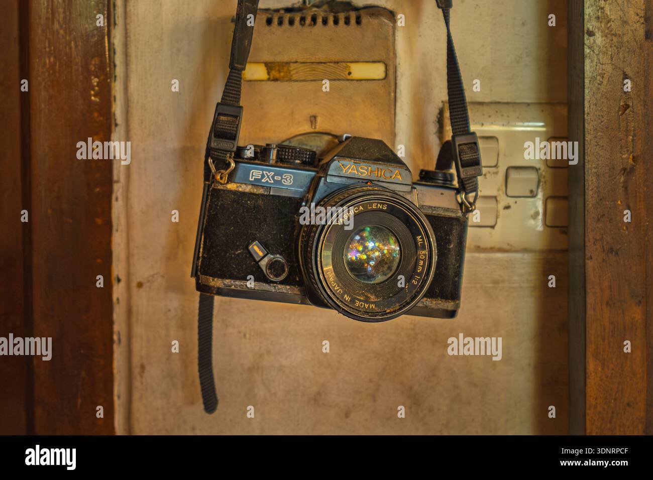 Balikpapan, Indonesien - 19. Dezember 2025. Eine nostalgische Nahaufnahme einer klassischen 35-mm-Yashica FX-3-Filmkamera mit einem 50-mm-Objektiv, das wieder an seinem Armband hängt Stockfoto
