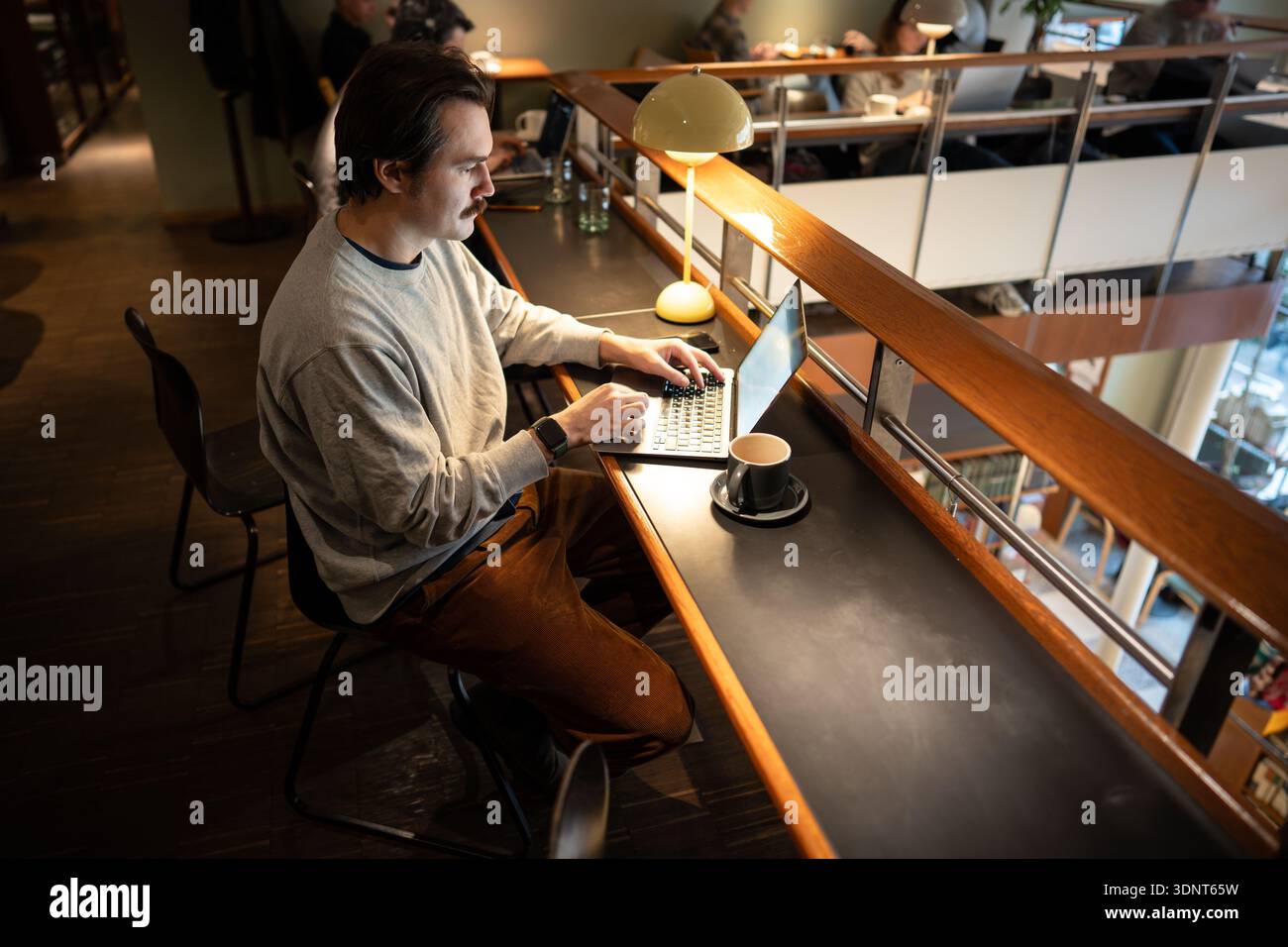 Positiver, entspannter Geschäftsmann, der an der Fernbedienung mit einem Laptop in einem trendigen Café arbeitet. Stockfoto