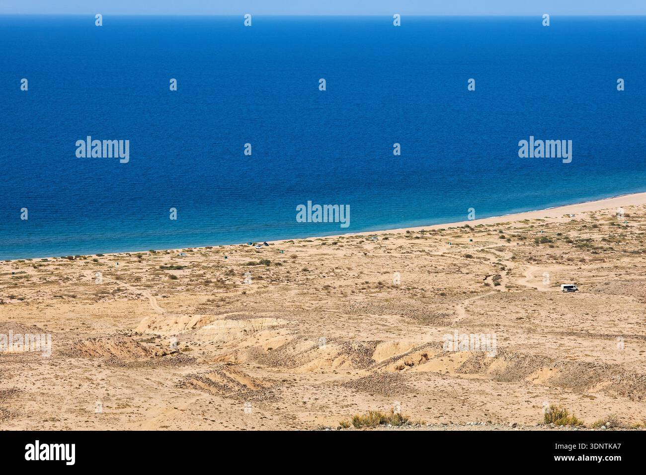 Blick aus der Vogelperspektive auf ein riesiges, ruhiges blaues Meer, das auf einen trockenen Sandstrand trifft. Broschüre für Reisen und Naturforschungen. Issyk Kul-See, Kirgisistan. Stockfoto
