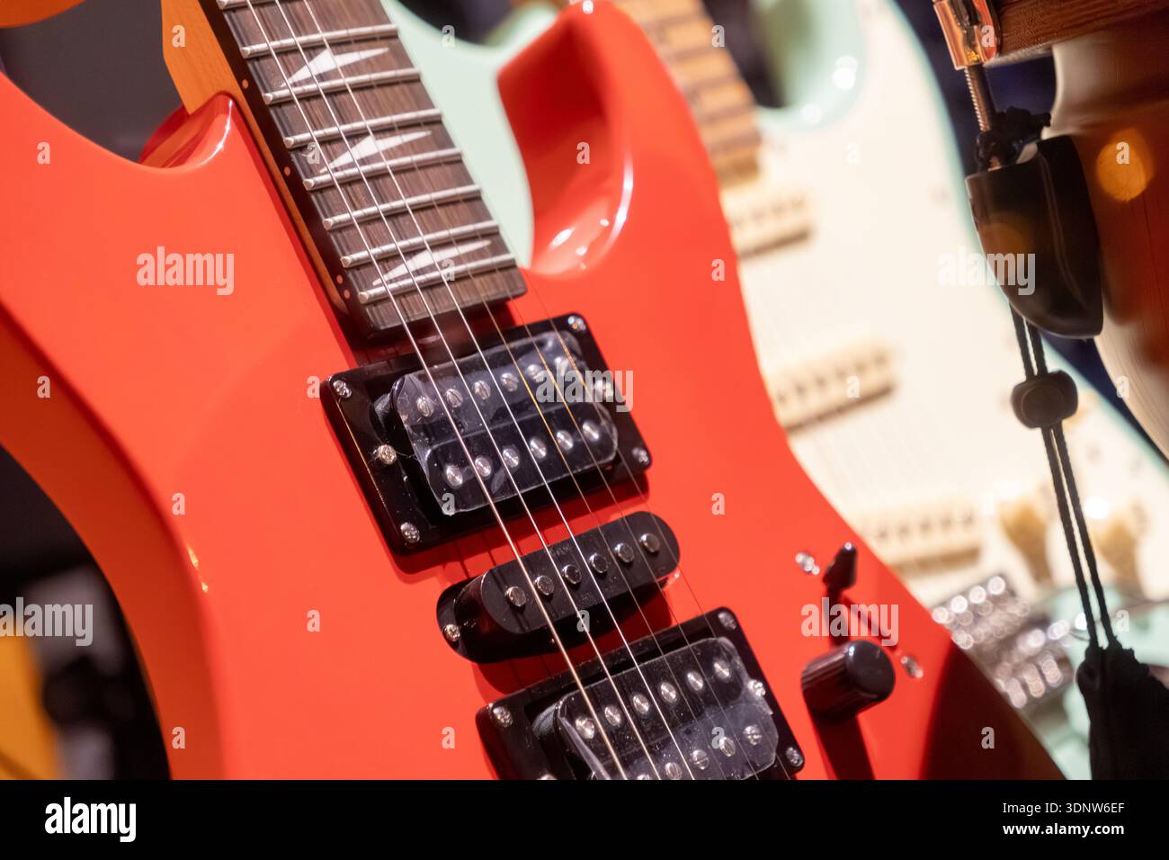 Detaillierte Ansicht einer leuchtend roten E-Gitarre mit glänzenden Streichern, schwarzen Humbucker-Tonabnehmern und poliertem Griffbrett für die Musikproduktion Stockfoto