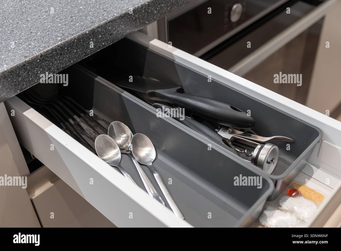 Nahaufnahme einer modernen Küchenschublade mit grauem Organizer mit glänzenden Löffeln, wichtigen Kochutensilien und kleinen Gegenständen Stockfoto