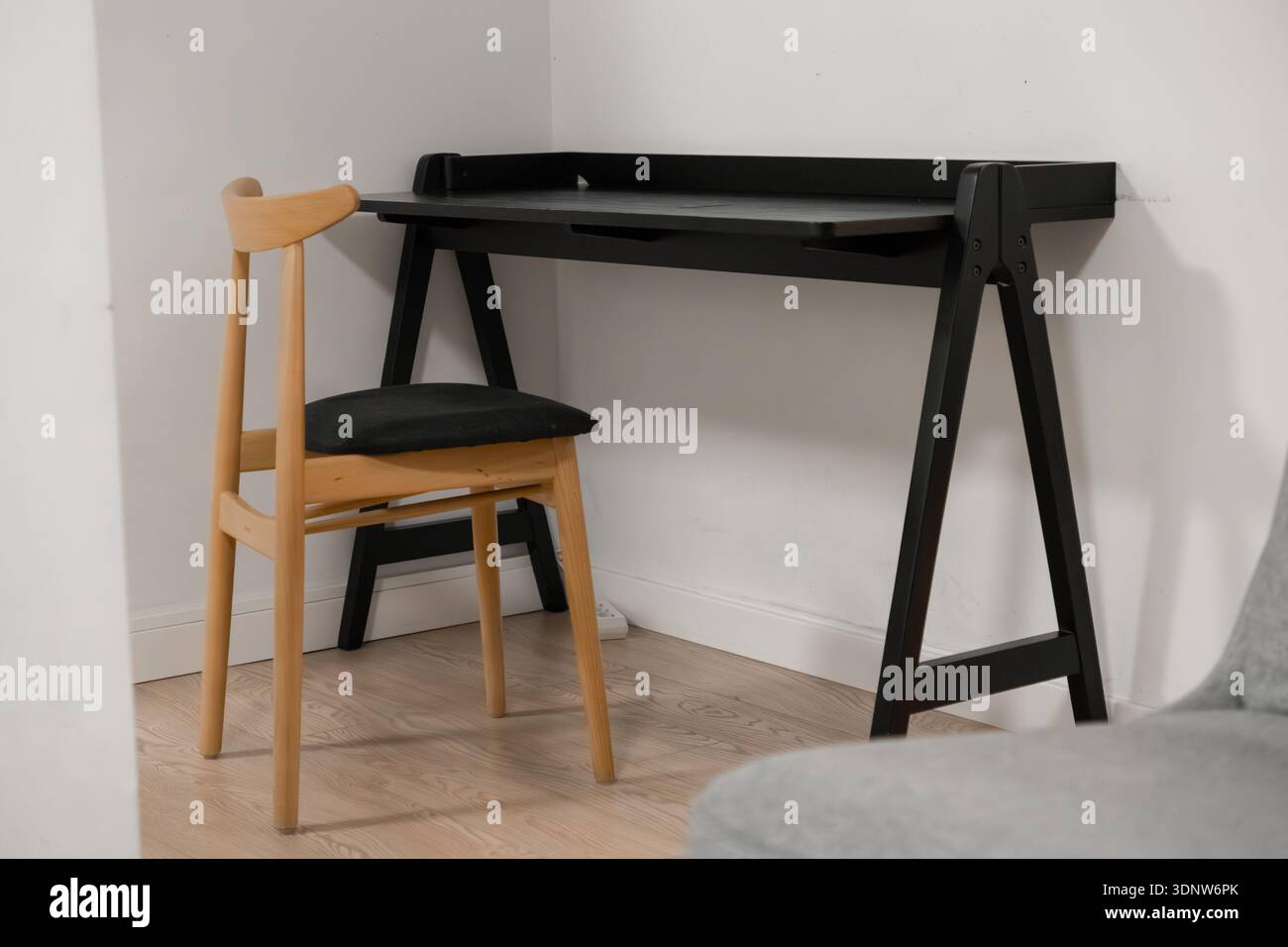 Blick auf einen einfachen schwarzen Schreibtisch mit hellem Holzstuhl, perfekt für ein modernes Heimbüro oder Arbeitszimmer, minimalistisches Dekor und effiziente Arbeitszimmer Stockfoto