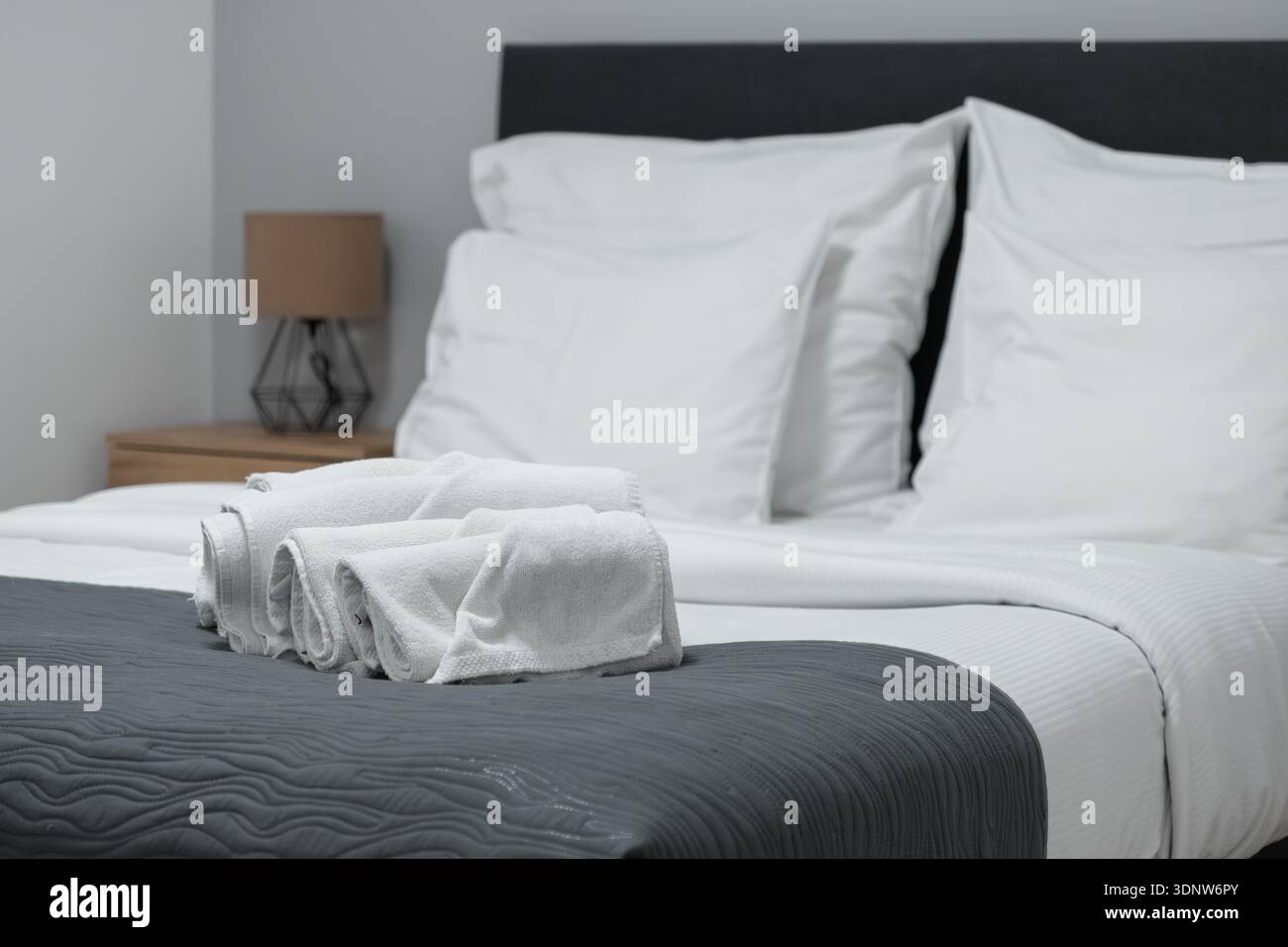 Nahaufnahme der frischen weißen Handtücher auf einer strukturierten grauen Decke auf einem sauberen Bett, die eine einladende Atmosphäre zum Entspannen und einen Pl. Bietet Stockfoto