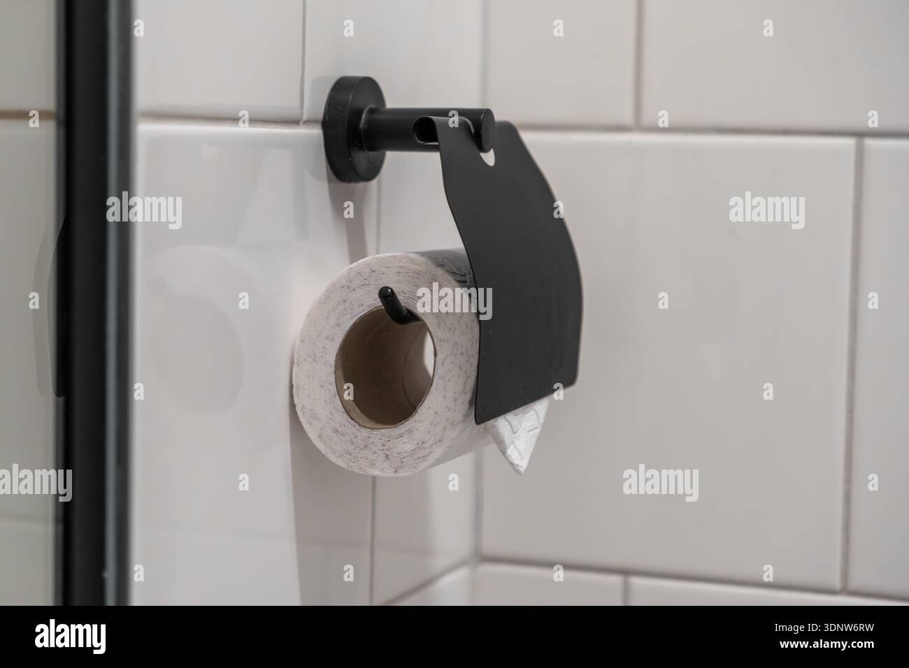 Nahaufnahme einer recycelten Toilettenpapierrolle, die sicher von einem eleganten schwarzen Spender gehalten wird und das zeitgenössische Design und die Notwendigkeit der persönlichen Pflege unterstreicht Stockfoto