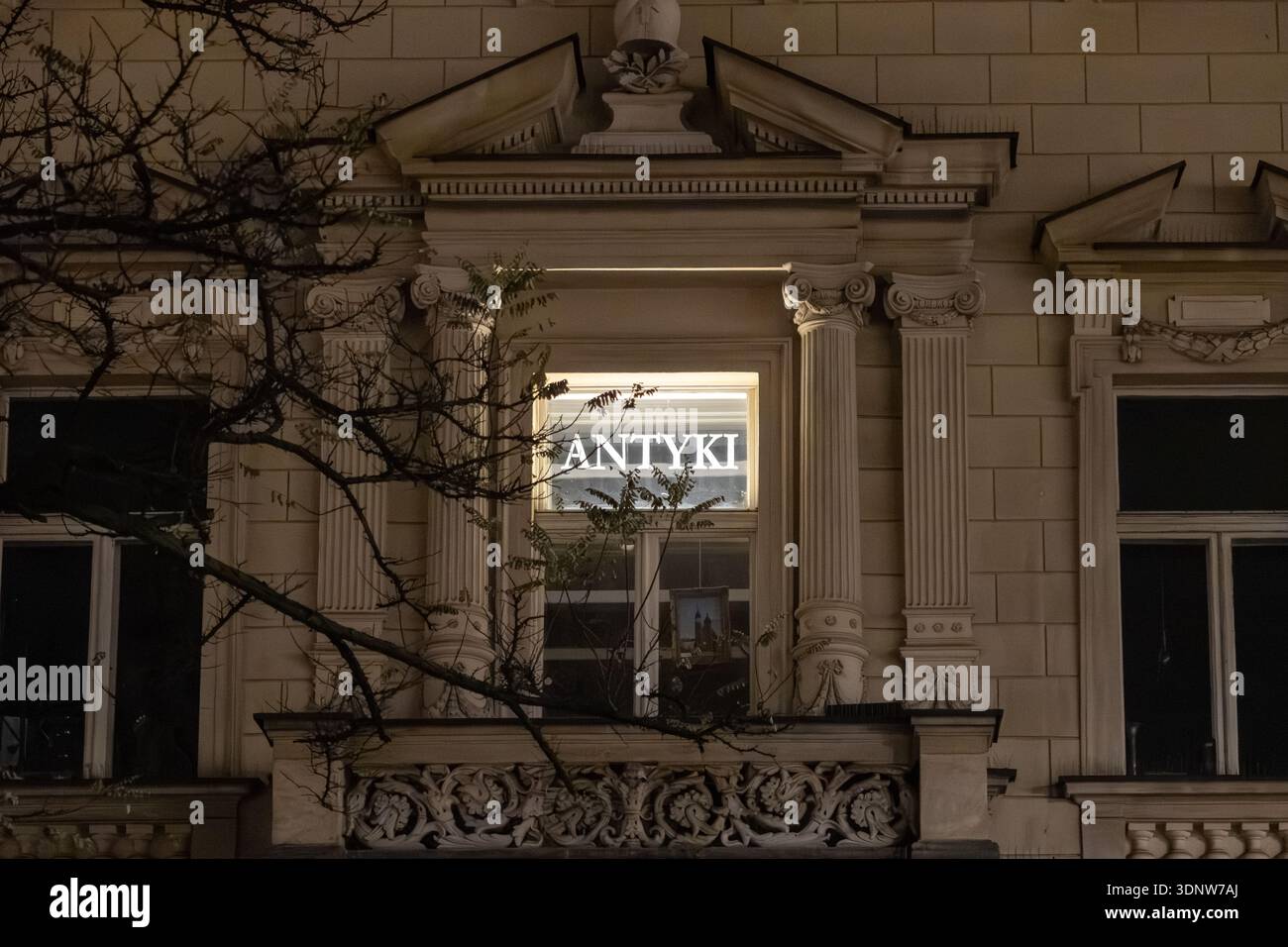 Krakau, Polen - 30. November 2025: Aufwendige architektonische Details eines historischen europäischen Gebäudes zeigen ein beleuchtetes ANTYKI-Schild in der Nacht, hoch Stockfoto