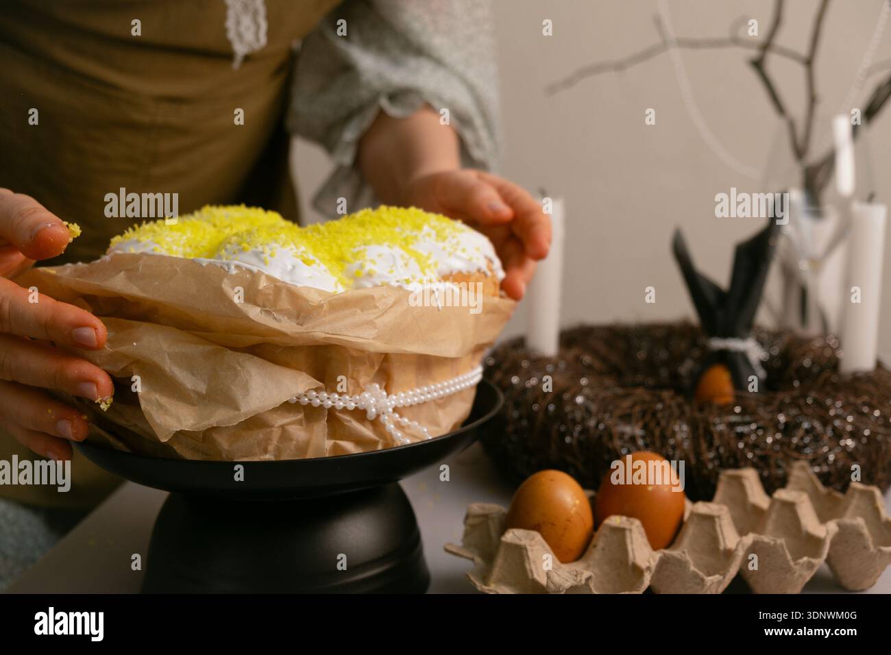 In Hauskleidung arrangiert sie Osterkuchen und bunte Eier auf dem Tisch und bereitet sie mit Liebe und Wärme zu. Stockfoto