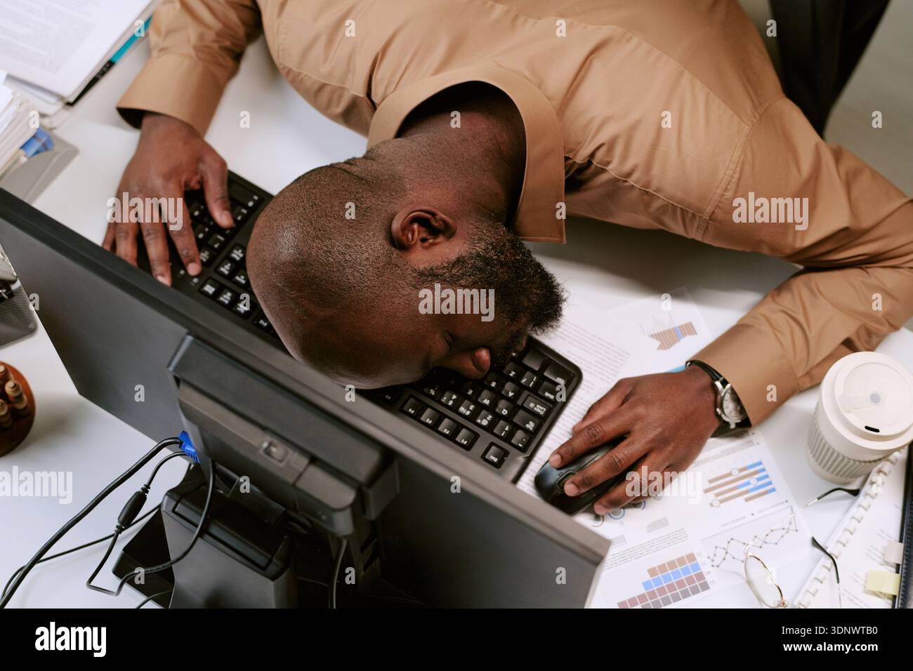 Junger schwarzer Mann, der während des Arbeitstages auf dem Schreibtisch schläft Stockfoto