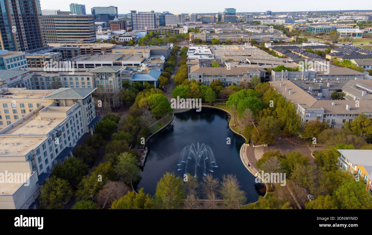 Aus der Vogelperspektive auf einen ruhigen Teich, der die Skyline reflektiert, umgeben von üppigem Grün und urbaner Architektur, die eine ruhige Oase in der Stadt, Plano, Stockfoto