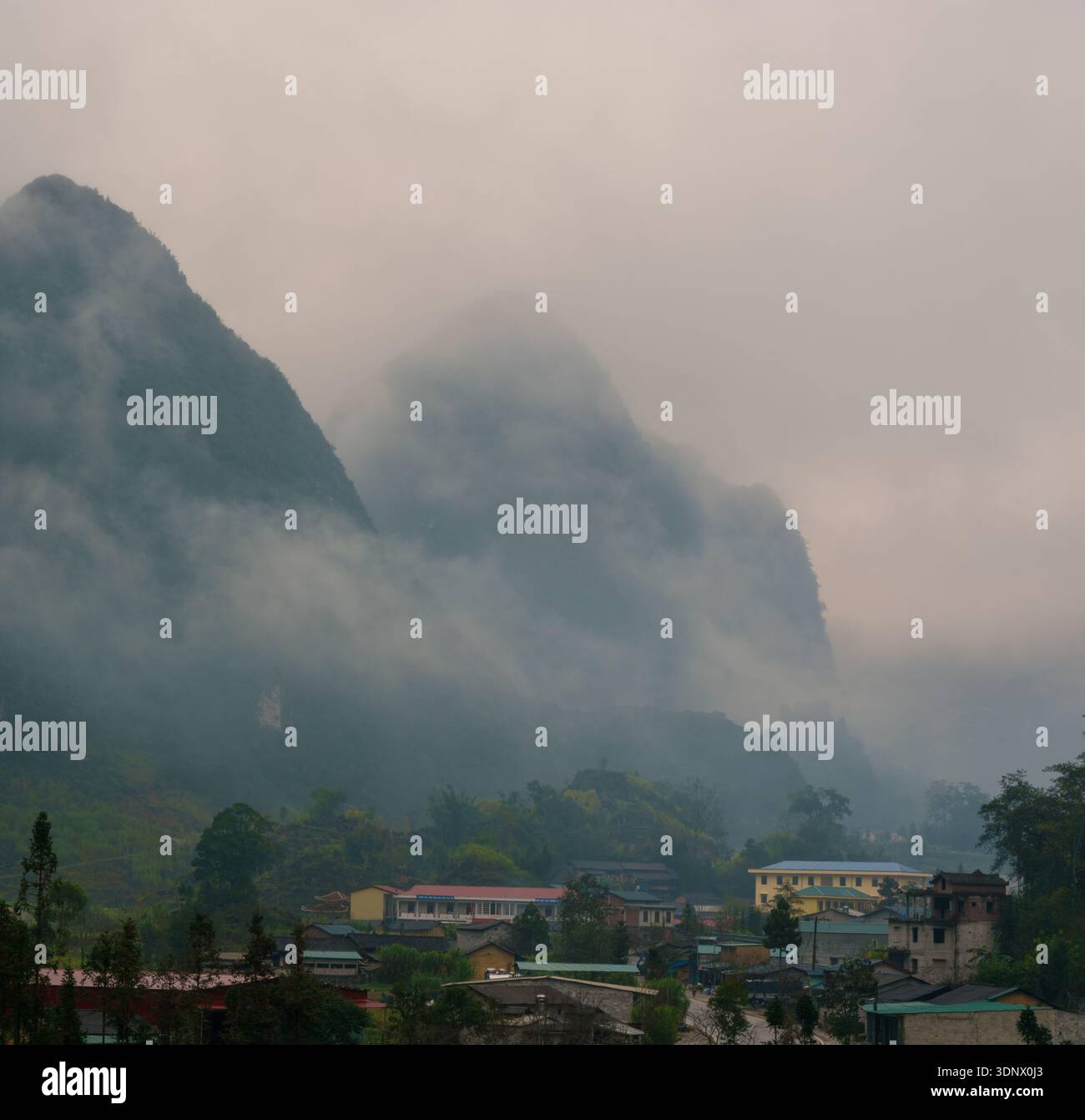 Ein ländliches Dorf liegt unter nebelbedeckten Karstbergen, die durch das warme Morgenlicht im Norden Vietnams gemildert werden. Stockfoto