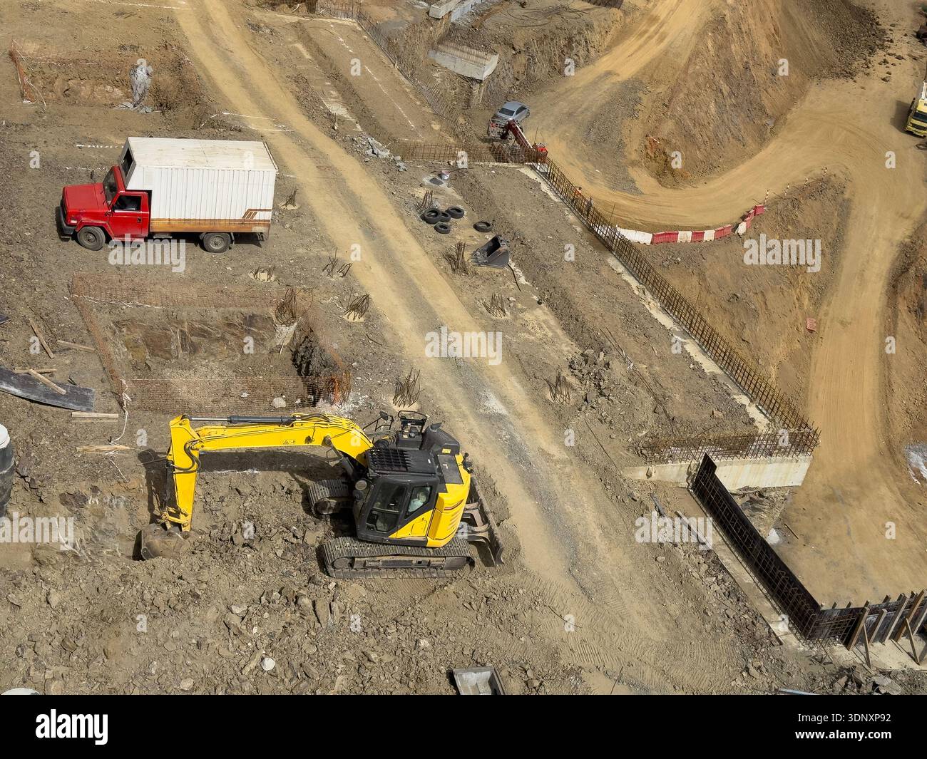 Luftaufnahme einer Baustelle mit einem gelben Planierschild, der aktiv Erde gräbt und bewegt, neben einem roten Lkw, der Maschinen und Sitzen zeigt Stockfoto