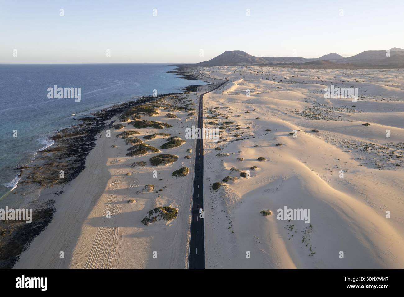 Aus der Vogelperspektive auf den starken Kontrast zwischen dem türkisfarbenen Meer und den goldenen Sanddünen entlang der Küste, Corralejo, Kanarischen Inseln, Spanien. Stockfoto