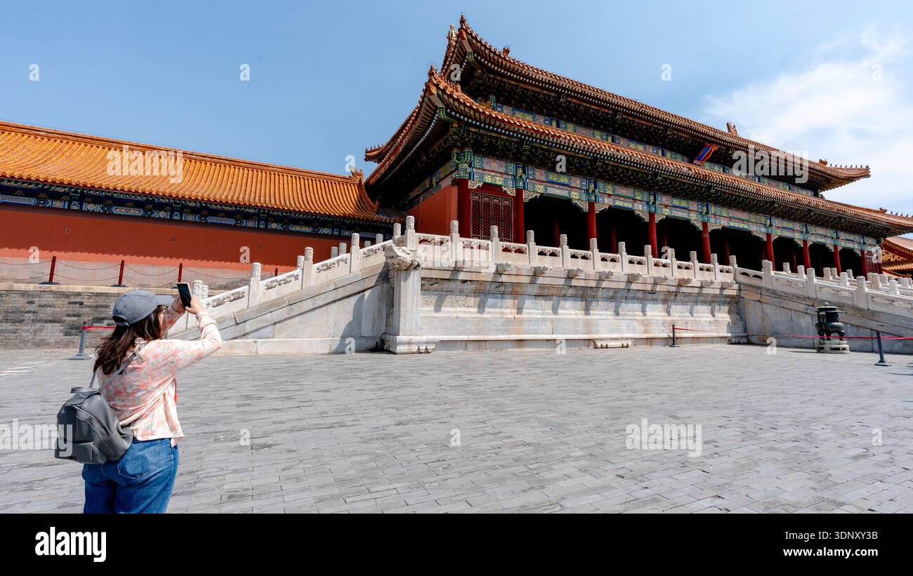 Eine weibliche Touristin fängt die kunstvolle Architektur von Pekings Verbotener Stadt ein und hebt komplexe Details und historische Pracht in einem klaren Blau hervor Stockfoto
