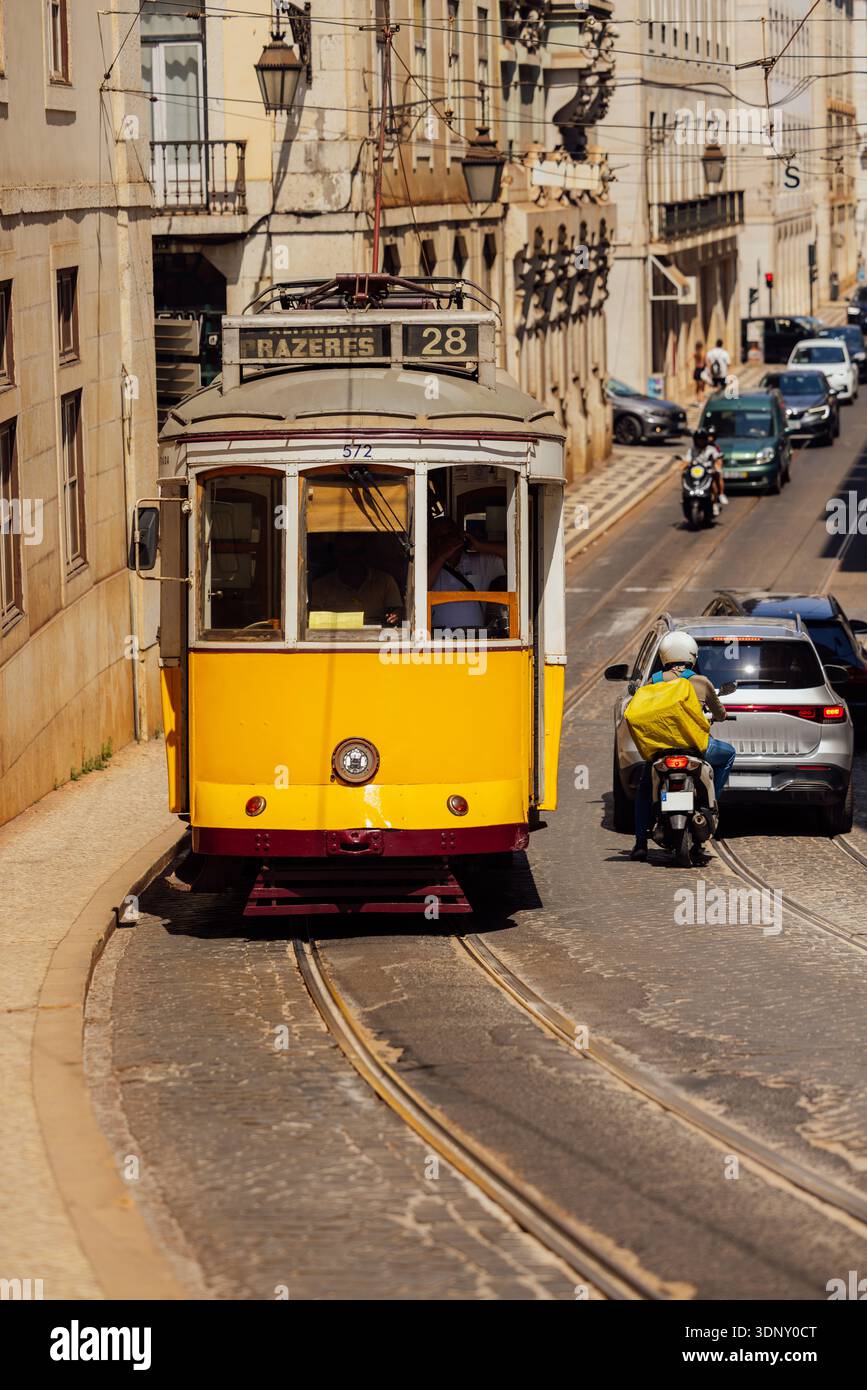 Eine lebhafte gelbe Straßenbahn 28 schlängelt sich durch die historischen Straßen von Lissabon, Portugal. An einem sonnigen Tag festgehalten, zeigt es den Charme von Bairro Alt Stockfoto
