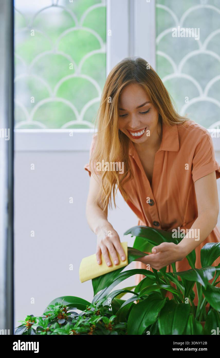 Eine Frau in einer entspannten häuslichen Umgebung, die sich mit Sorgfalt um ihre Zimmerpflanzen kümmert. Die ruhige Umgebung unterstreicht ihre Freude an einem friedlichen Lebensstil A Stockfoto