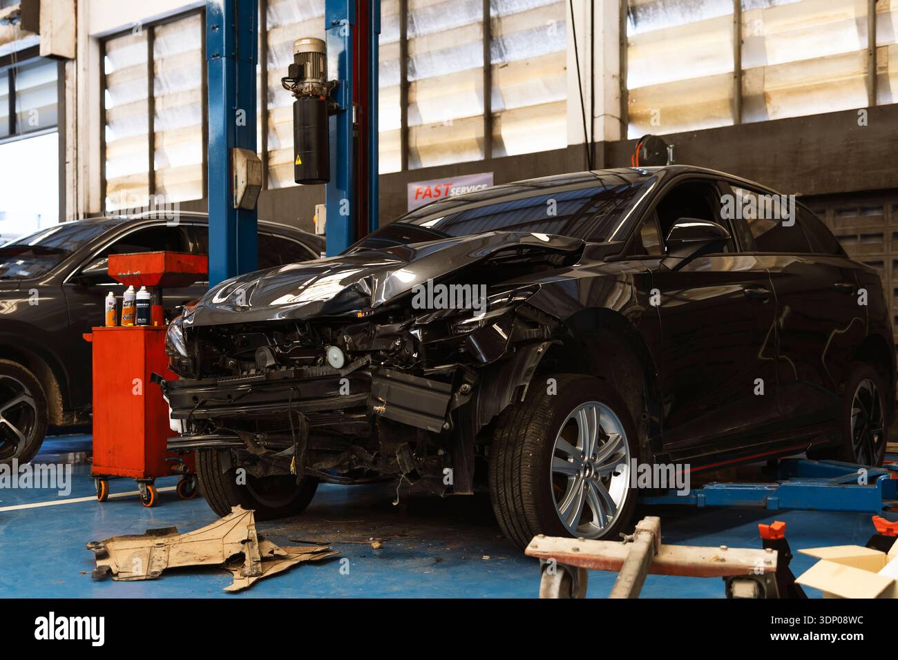 Beschädigtes schwarzes Fahrzeug mit zerknitterter Motorhaube und fehlendem Stoßfänger in einer Garage für Kollisionsreparaturen und Versicherungsansprüche. Stockfoto