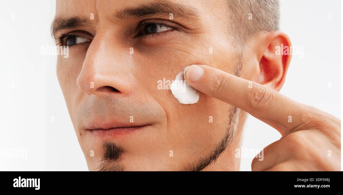 Eine Nahaufnahme eines attraktiven Mannes mit gesunder Haut, die Anti-Falten oder Anti-Aging-Creme aufträgt. Stockfoto