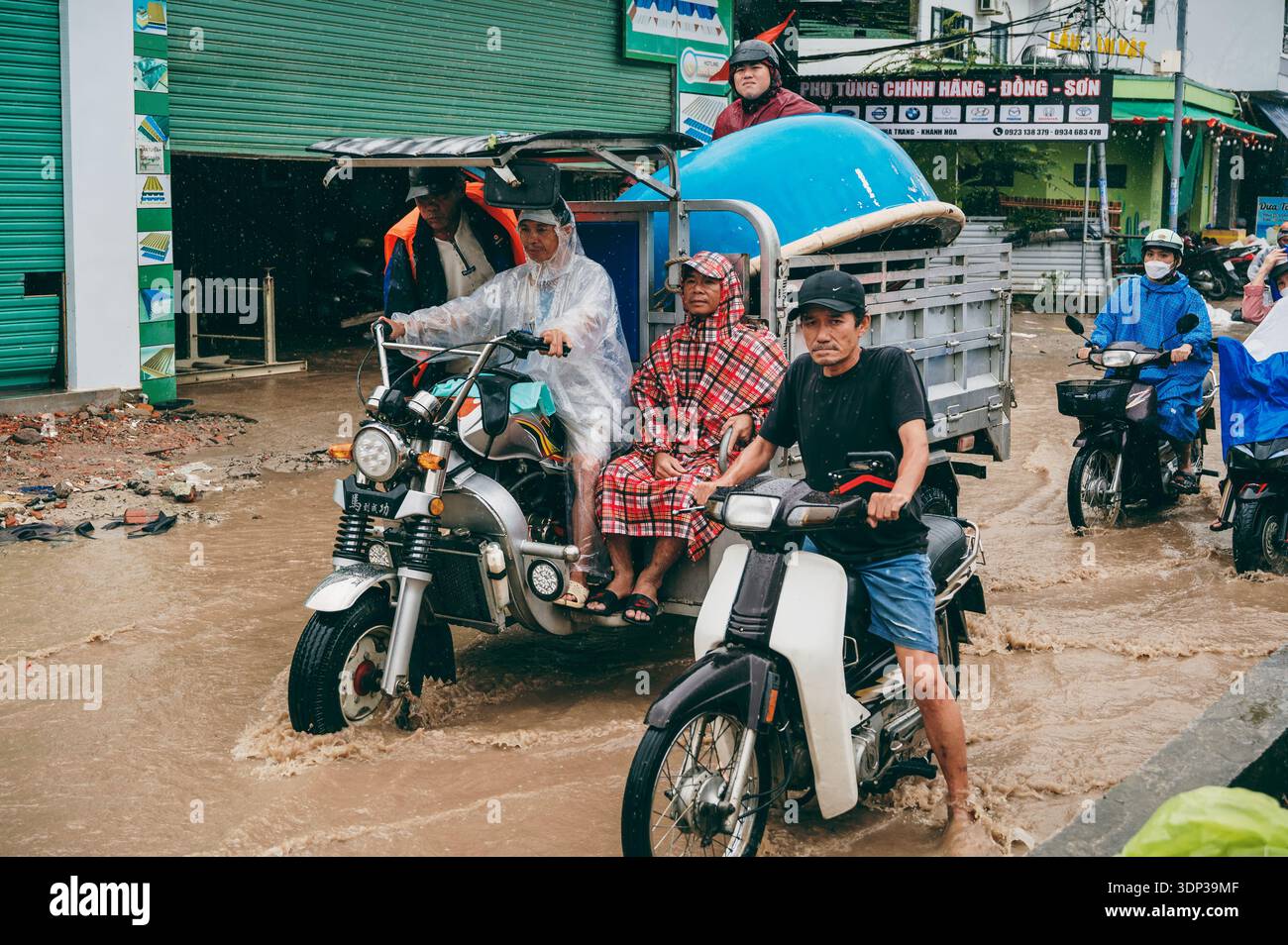 Eine Straßenszene, in der Menschen Motorräder auf einer überfluteten Straße bei starkem Regen in Nha Trang fahren. Nha Trang, Vietnam - 21. November 2025. Stockfoto