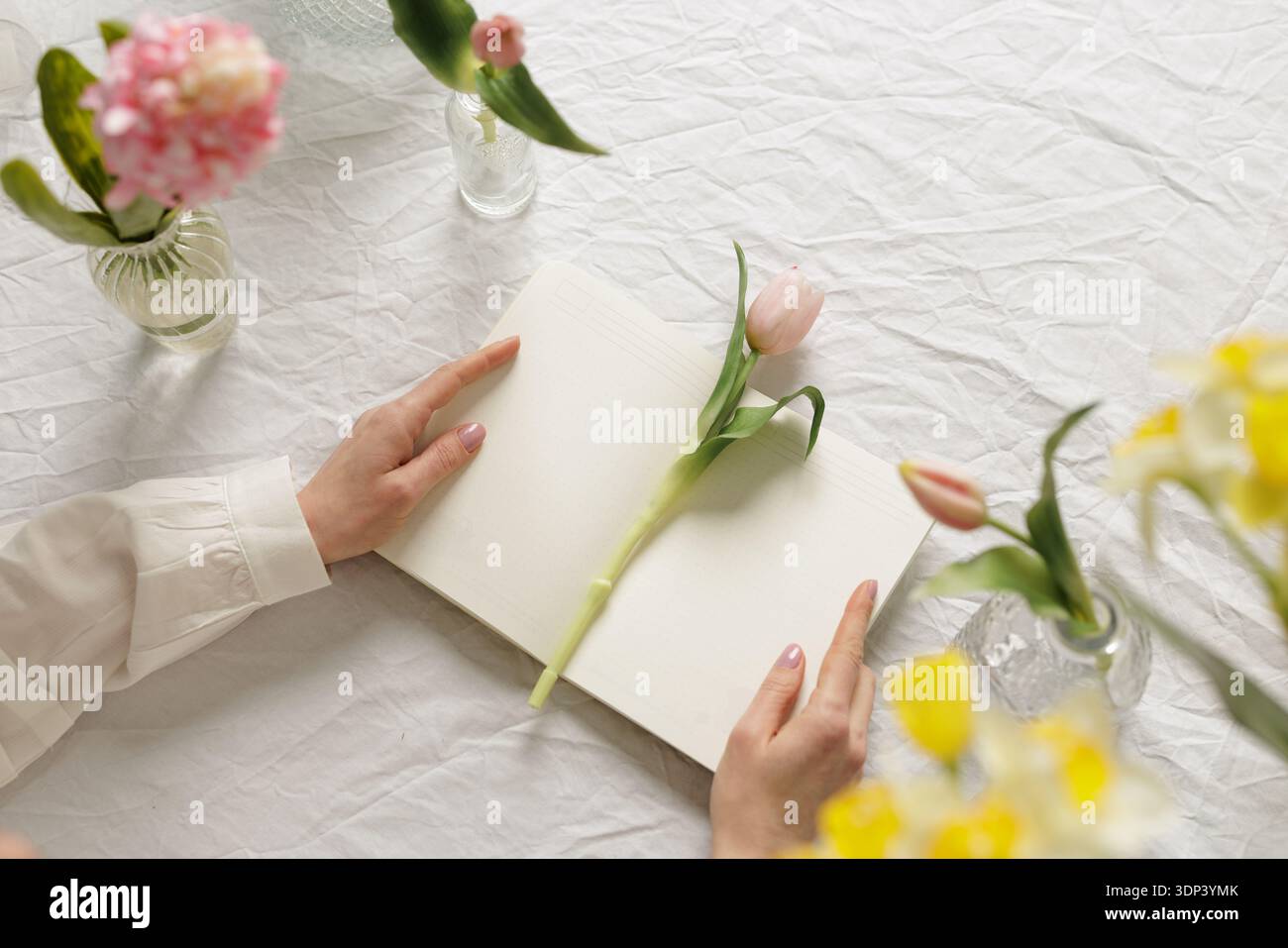 Draufsicht des offenen Notizbuchs mit Tulpen und Frühlingsblumen auf dem Tisch. Ideal für Floristik-Branding, saisonale Kampagnen und kreative Marketinginhalte. Stockfoto