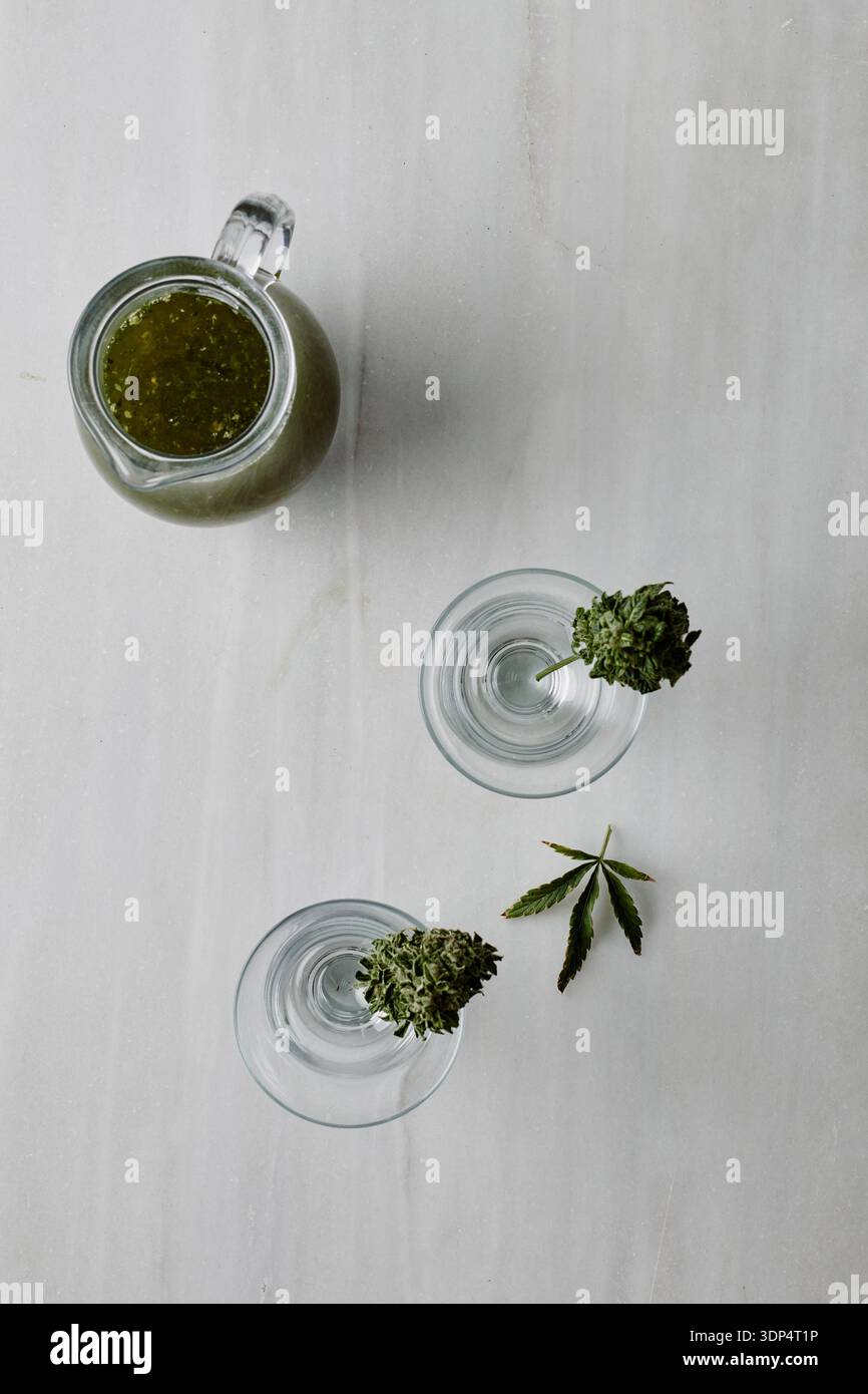 Grüner, mit Cannabis angereicherter Cocktail in Gläser auf Marmortisch gießen Stockfoto
