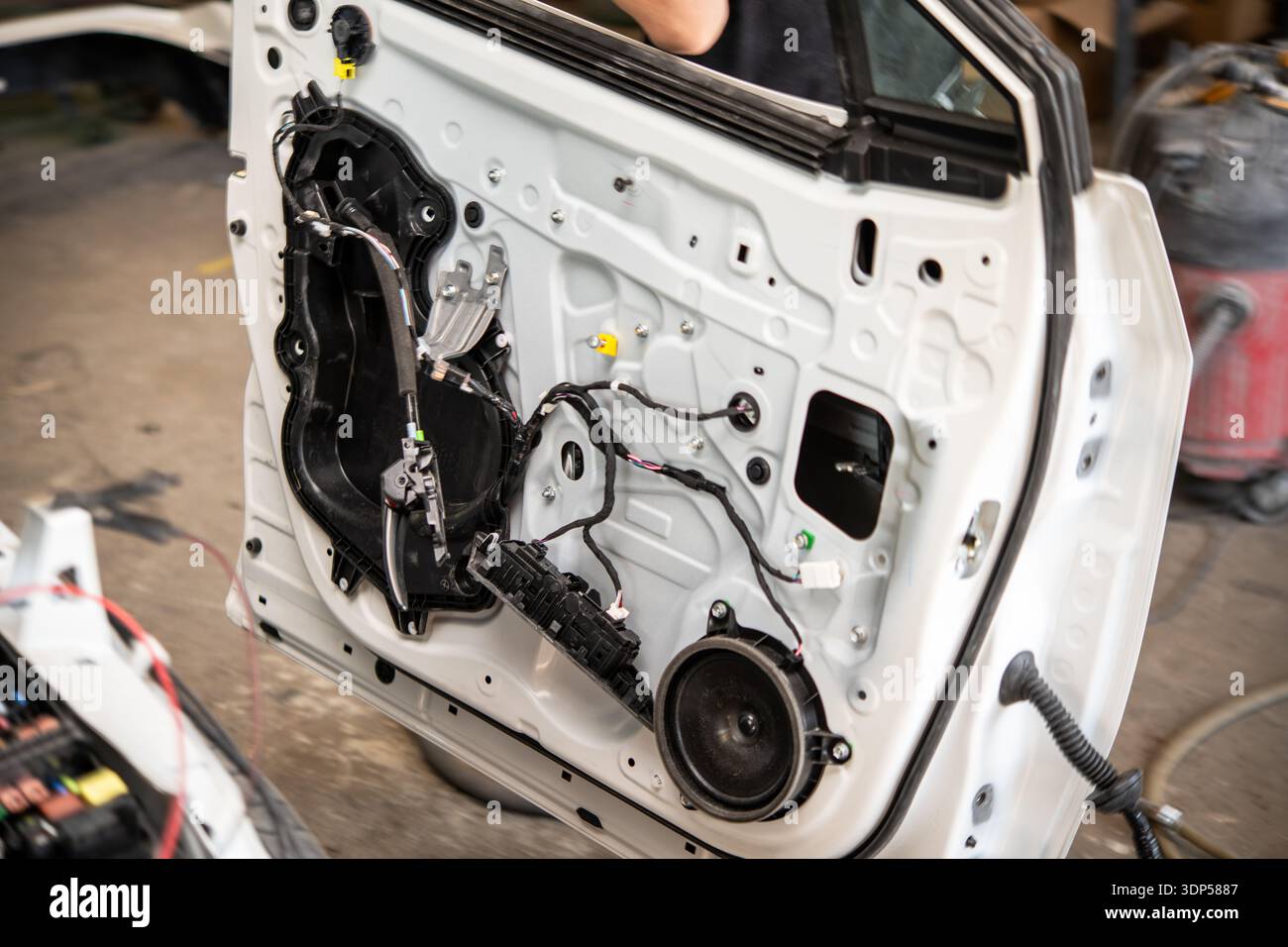 Die Kfz-Türverkleidung mit freiliegender Verkabelung und Lautsprecher wird in einer Karosseriebau repariert, im Hintergrund befinden sich Werkzeuge und Ausrüstung. Stockfoto