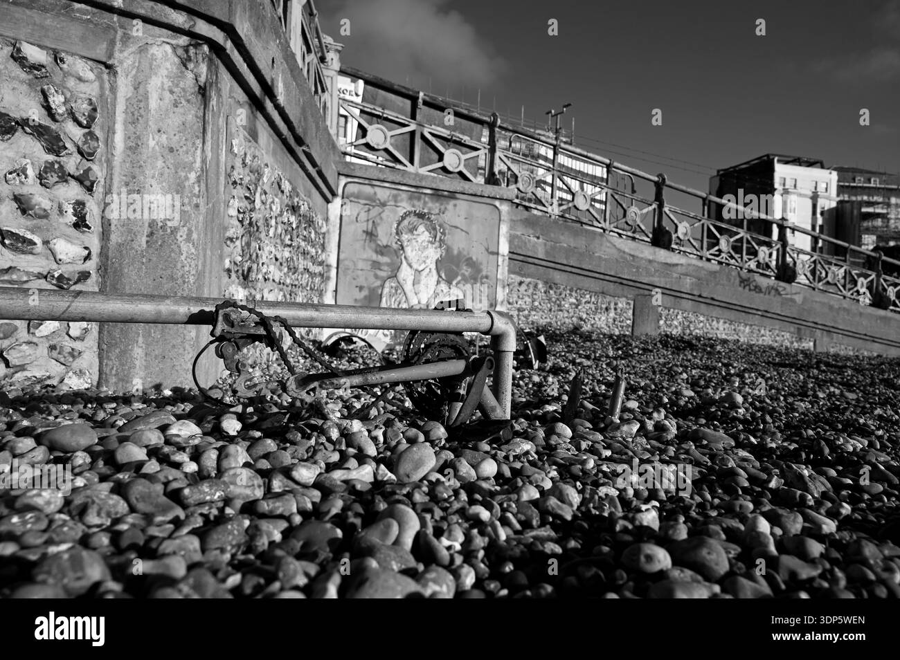 Altes, verlassenes Fahrrad, das nach den letzten Winterstürmen 2026 in schwarz-weiß in Schindeln am Brighton Beach mit Schindeln bedeckt war, Großbritannien: Credit Simon Dack Stockfoto