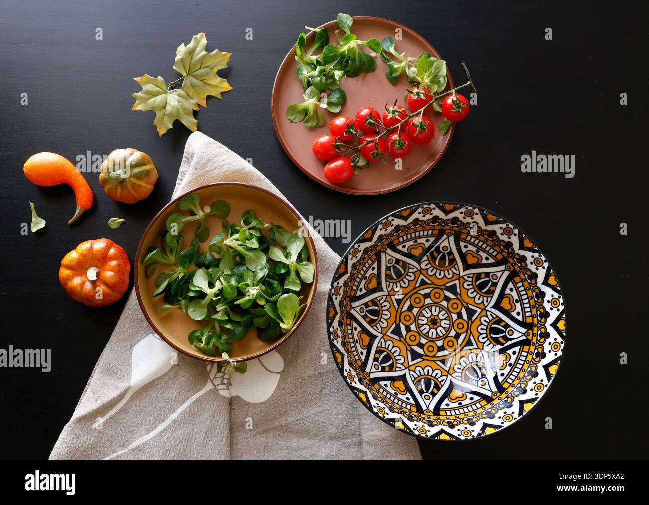 Mehrfarbige Keramikplatten und gemusterte Schüssel mit Gemüse und Kräutern auf schwarzem Hintergrund. Essen und traditionelle Küche. Draufsicht. Stockfoto