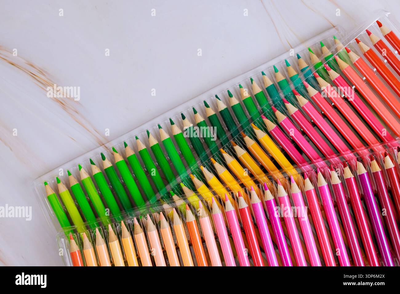 Farbige Bleistifte in verschiedenen Farben werden ordentlich in einer durchsichtigen Hülle auf einer hellen Oberfläche platziert. Stockfoto