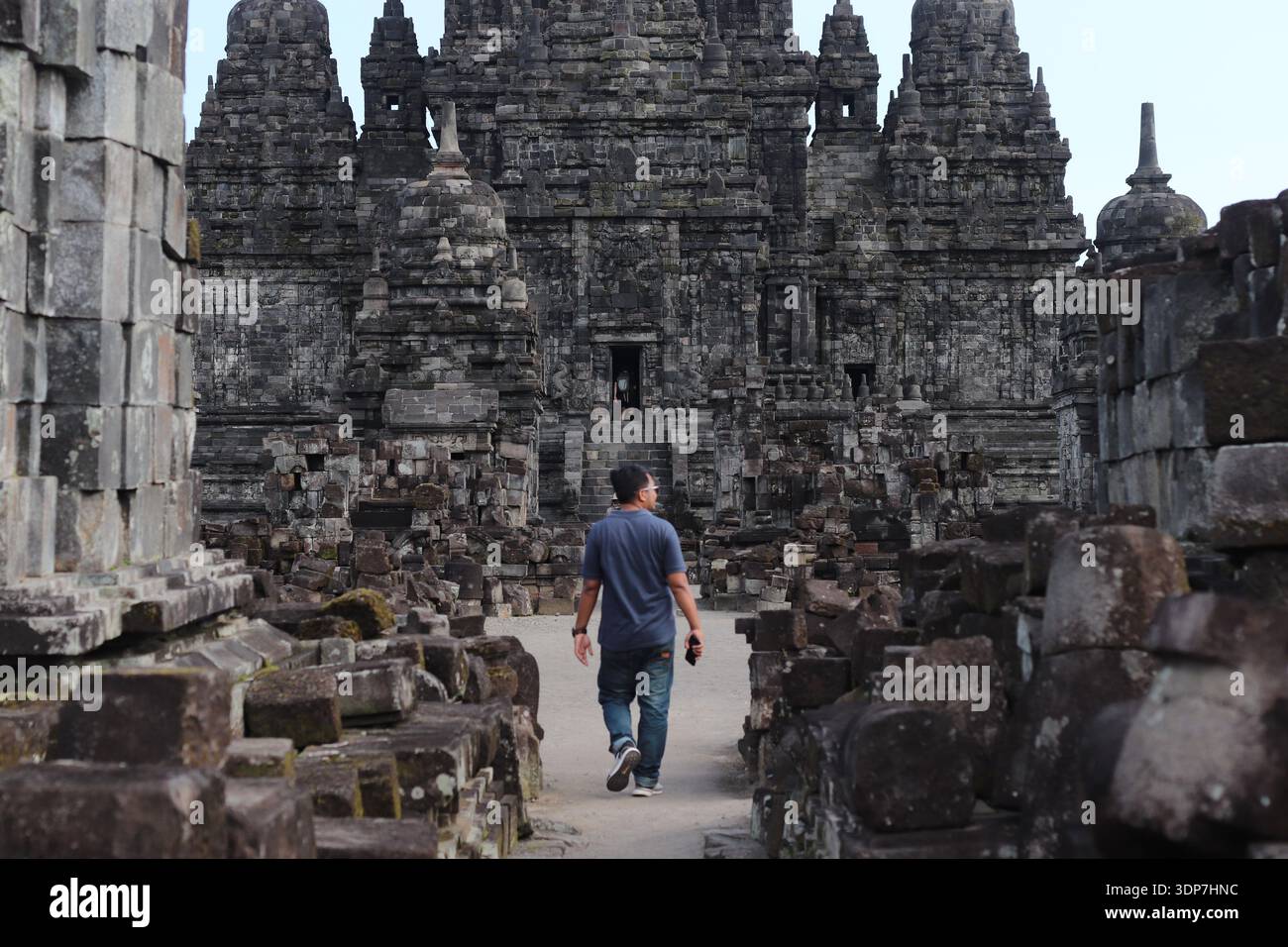 Ein einsamer Besucher spaziert durch den alten Steinkorridor von Candi Prambanan, umgeben von hoch aufragenden Tempelmauern und verwitterten Ruinen. Der strukturierte ston Stockfoto