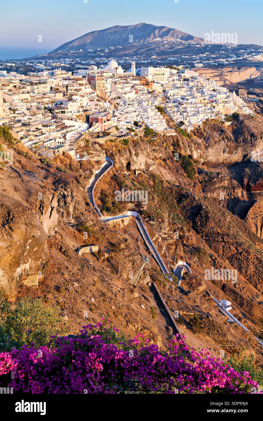 Fira, Santorini, Griechenland, bei Sonnenuntergang. Weiße Gebäude kaskadieren die Caldera-Klippe hinunter, verbunden durch gewundene Wege und eine Seilbahn, die einen atemberaubenden Blick bietet Stockfoto