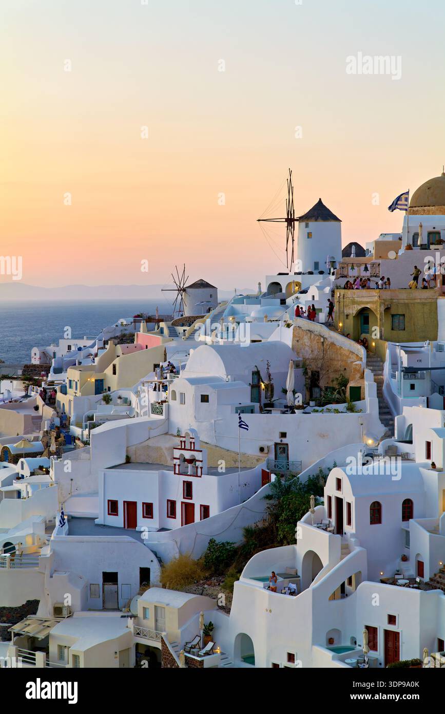 Touristen treffen sich in Oia, Santorin, Griechenland, um den berühmten Sonnenuntergang über der Ägäis zu erleben, umgeben von traditionellen weiß getünchten Gebäuden und Wind Stockfoto