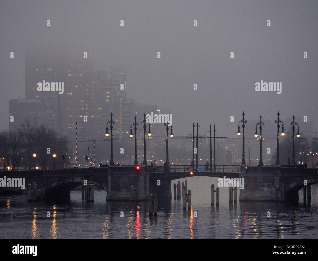 Amsterdam, Niederlande - 20. Januar 2025: Nächtliches, nebeliges Amsterdamer Stadtbild mit einer Kanalbrücke mit kunstvollen Straßenlaternen und beleuchteten Gebäuden Stockfoto