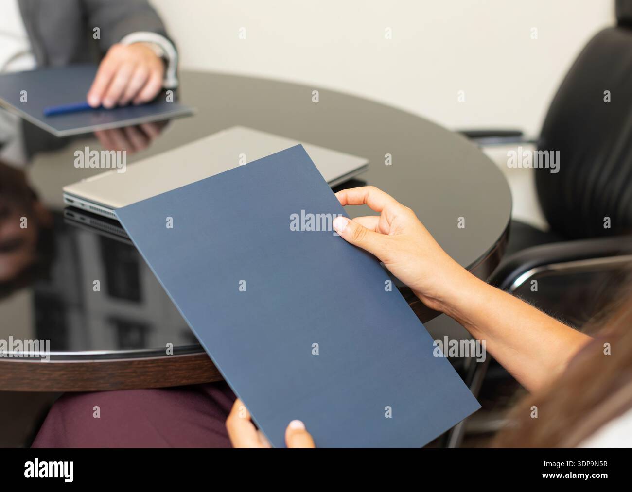 Zwei Leute sitzen an einem runden Tisch in einem Büro. Eine Person hält einen Ordner, die andere sitzt mit einem Laptop. Sie diskutieren wahrscheinlich über wichtiges Busin Stockfoto