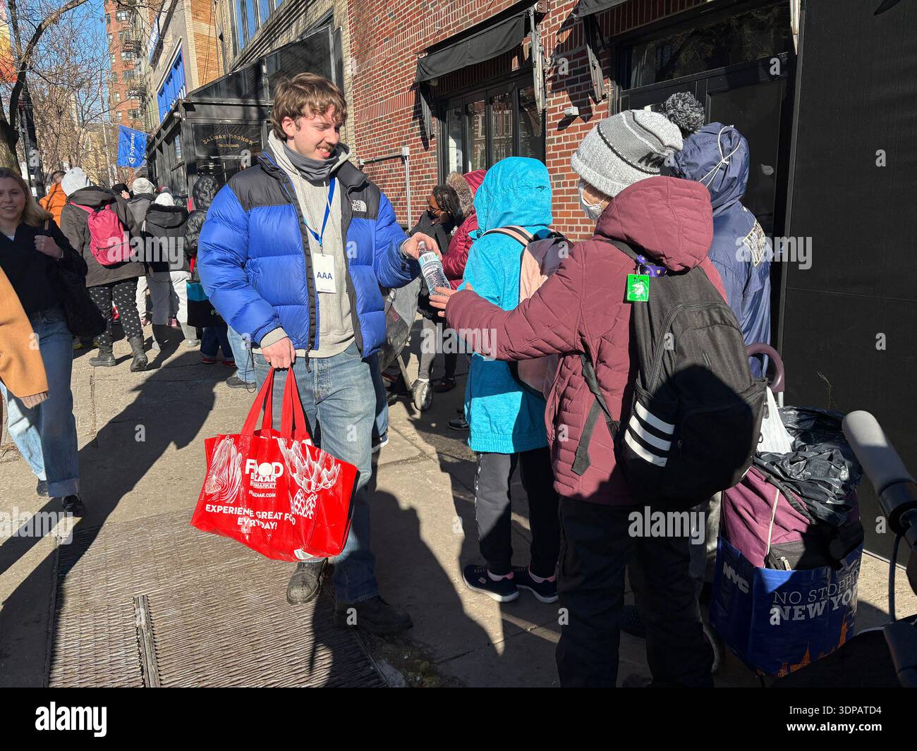 Ein Mitarbeiter von Polymarket gibt kostenlose Flaschen Wasser an Personen aus, die vor dem Geschäft in der Schlange stehen. Das Lokal wurde heute um 14:00 Uhr offiziell eröffnet, für das, was „New Yorks erstes kostenloses Lebensmittelgeschäft“ im West Village heißt. Die Tickets wurden Stunden vorher ausgehändigt und viele Käufer begannen um 7 Uhr morgens in der Schlange zu stehen. Sie bekamen eine Tasche und konnten die Tüte bis zum Rand mit kostenlosen Lebensmitteln füllen. Quelle: SOPA Images Limited/Alamy Live News Stockfoto