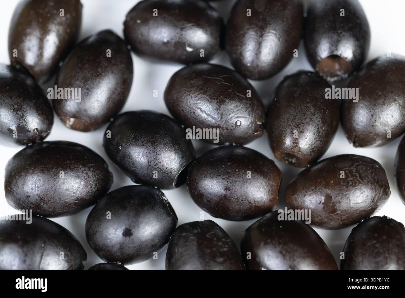 Makroglitzernde schwarze Oliven mit Tropfen, gesalzen in pikanter Salzlake mit reichhaltigem Ölglanz, erinnern an mediterrane Tapas-Szene, perfekte Garnitur für Appetit Stockfoto