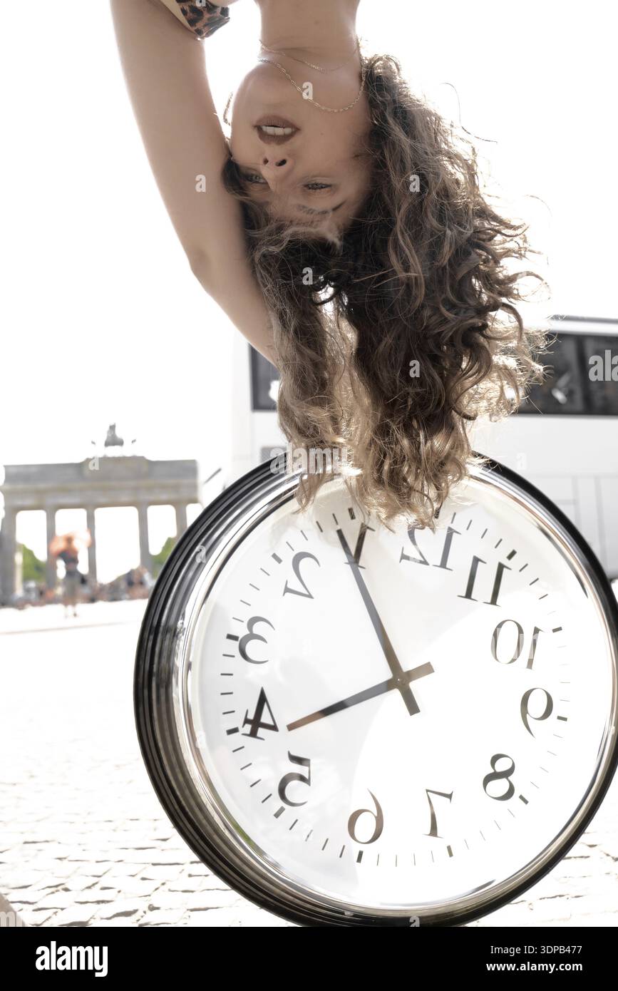 Frau, die kopfüber neben einer großen Uhr mit historischer Architektur des Brandenburger Tors in Berlin steht, Zeitsprung, Zeitverzug, Transtemp Stockfoto