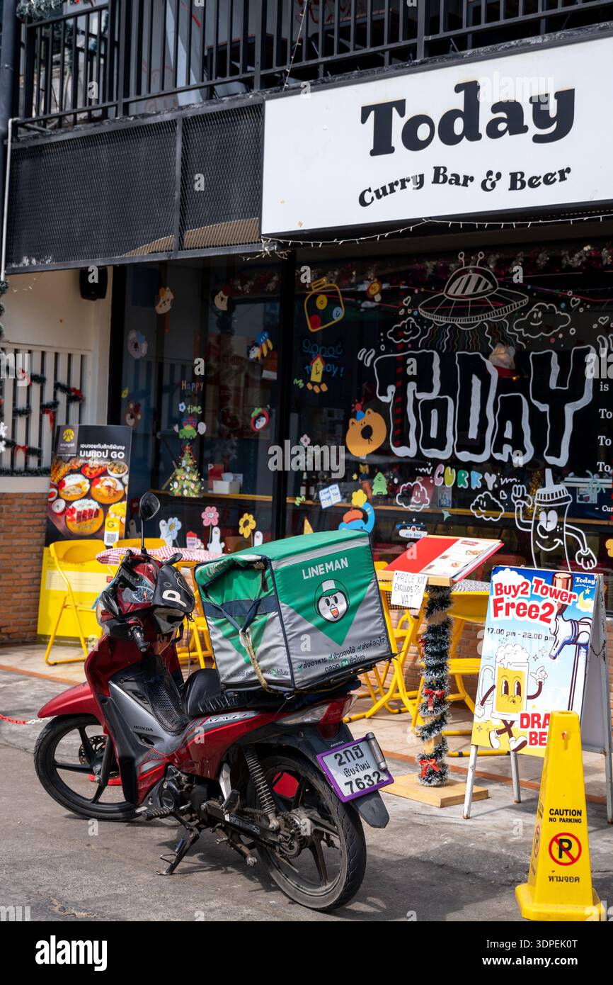 Ein roter Roller mit grüner Lieferbox steht vor dem Restaurant „Today Curry Bar & Beer“ in Thailand. Diese Straßenszene tagsüber Stockfoto