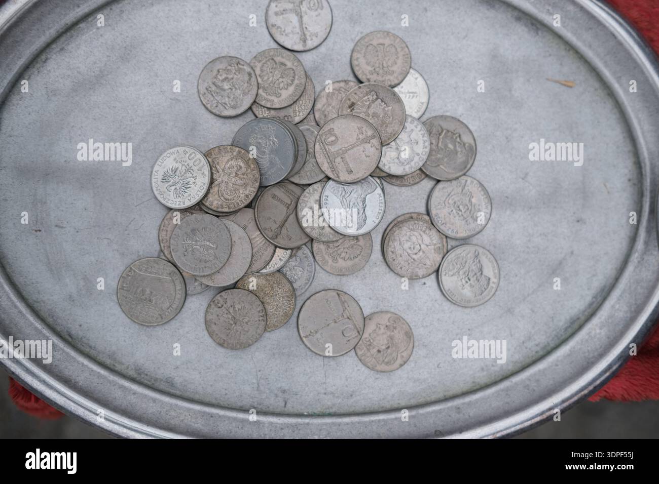 Ansicht von oben nach unten auf mehrere silberfarbene Münzen mit Reliefporträts und Inschriften, die in einer runden Metallschale mit erhöhtem Rand verstreut sind Stockfoto