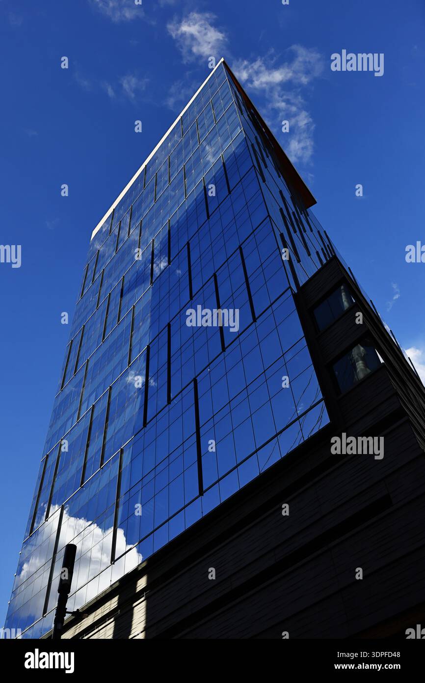 Der niedrige Winkel eines blauen Glasgebäudes zeigt dünne vertikale Fensterschlitze und Wolkenreflexionen entlang der Fassade an der Ecke in Denver, Colorado, USA. Stockfoto
