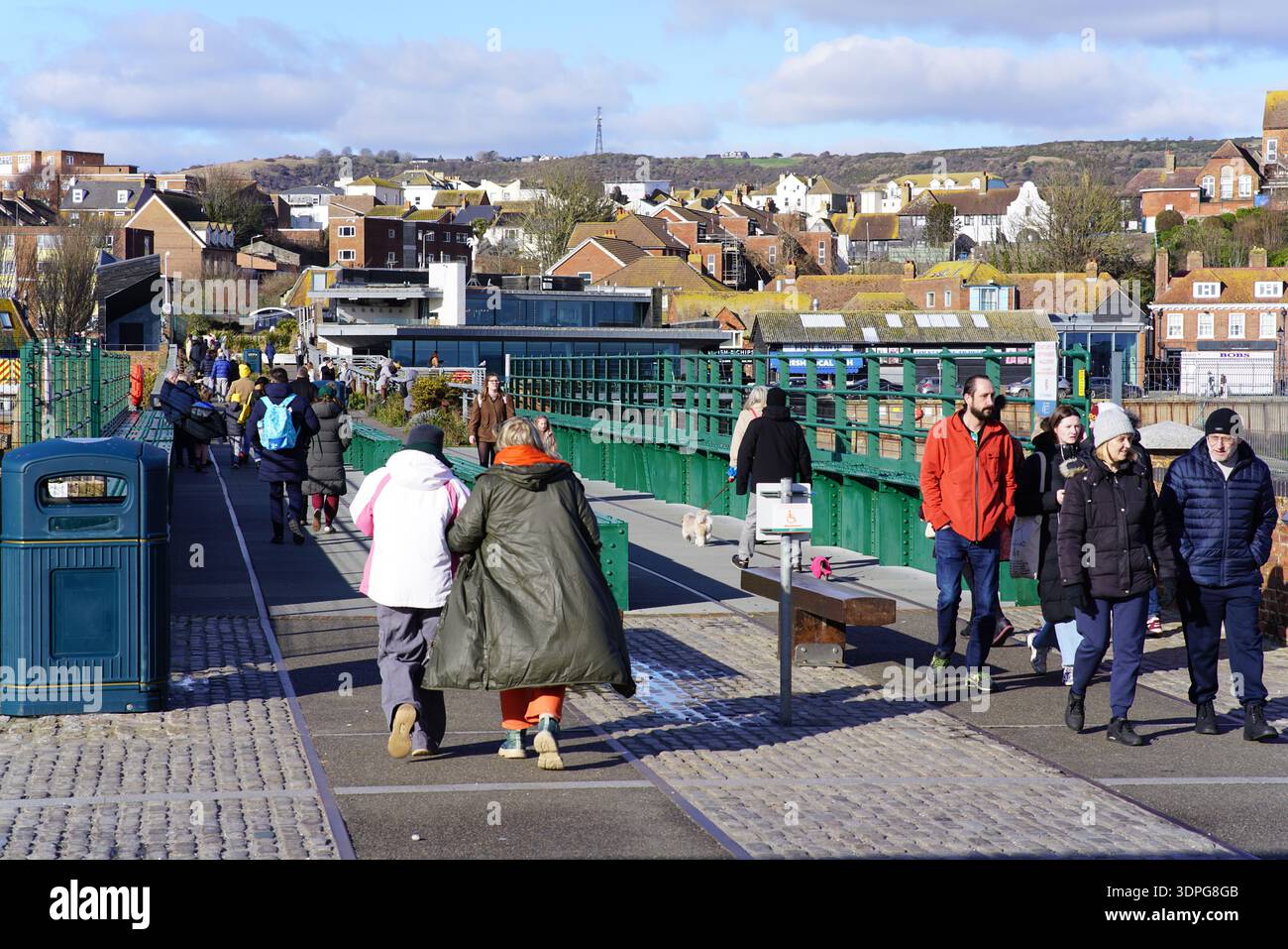 Menschenmassen laufen auf der grünen Fußgängerbrücke am Folkestone Harbour Arm Link, Wintermäntel und sonnige Aussicht auf die Stadt, Kent England Küste. Folkestone Stockfoto