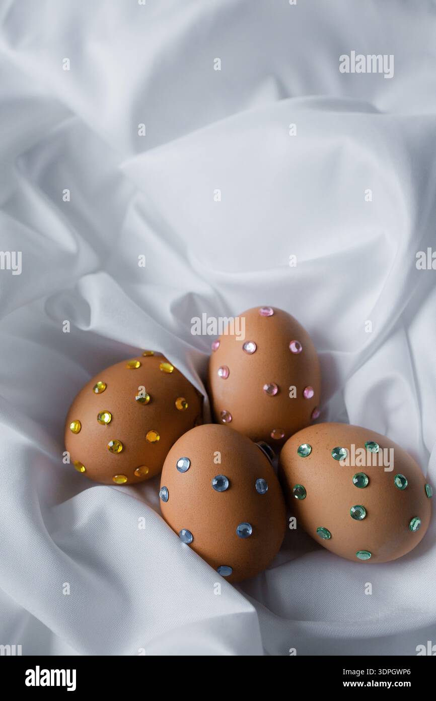 Ostereier mit Glitzersteinchen auf weißem Seidenstoff. Osterfeierstraditionen, Designideen für Kinder. Stockfoto