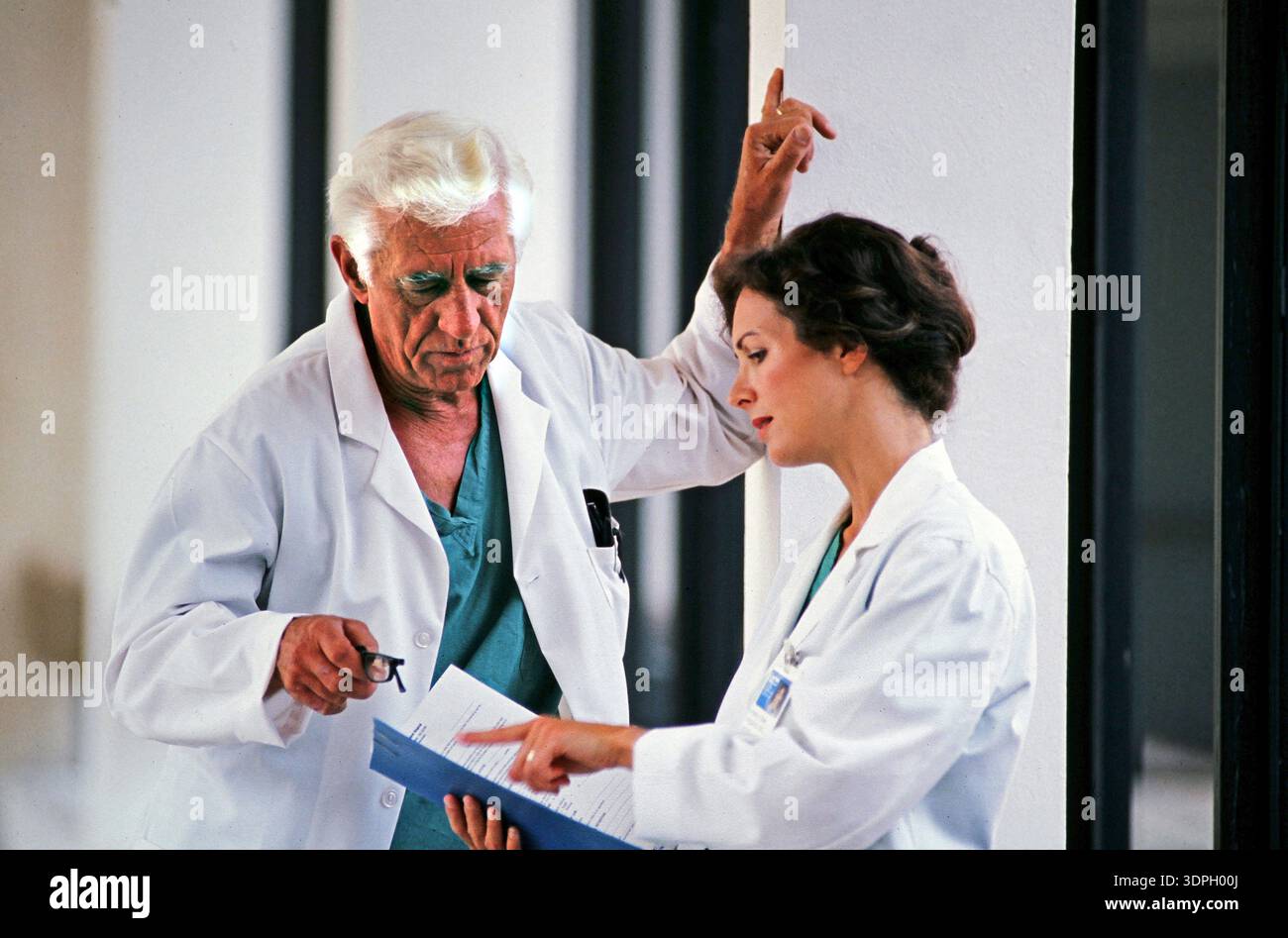 Zwei Ärzte führen ein Gespräch, während sie eine Patientenakte in einem Krankenhaus überprüfen. Sie konzentrieren sich auf die Details im Dokument und heben deren hervor Stockfoto