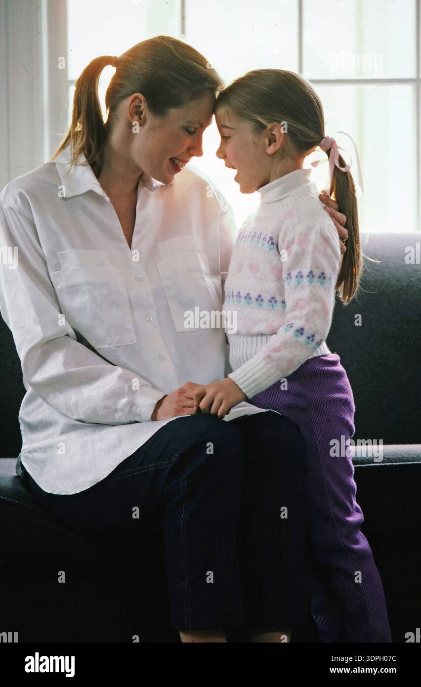 Eine Mutter und Tochter berühren ihre Köpfe, während sie einen zarten Moment in ihrem Zuhause genießen Stockfoto