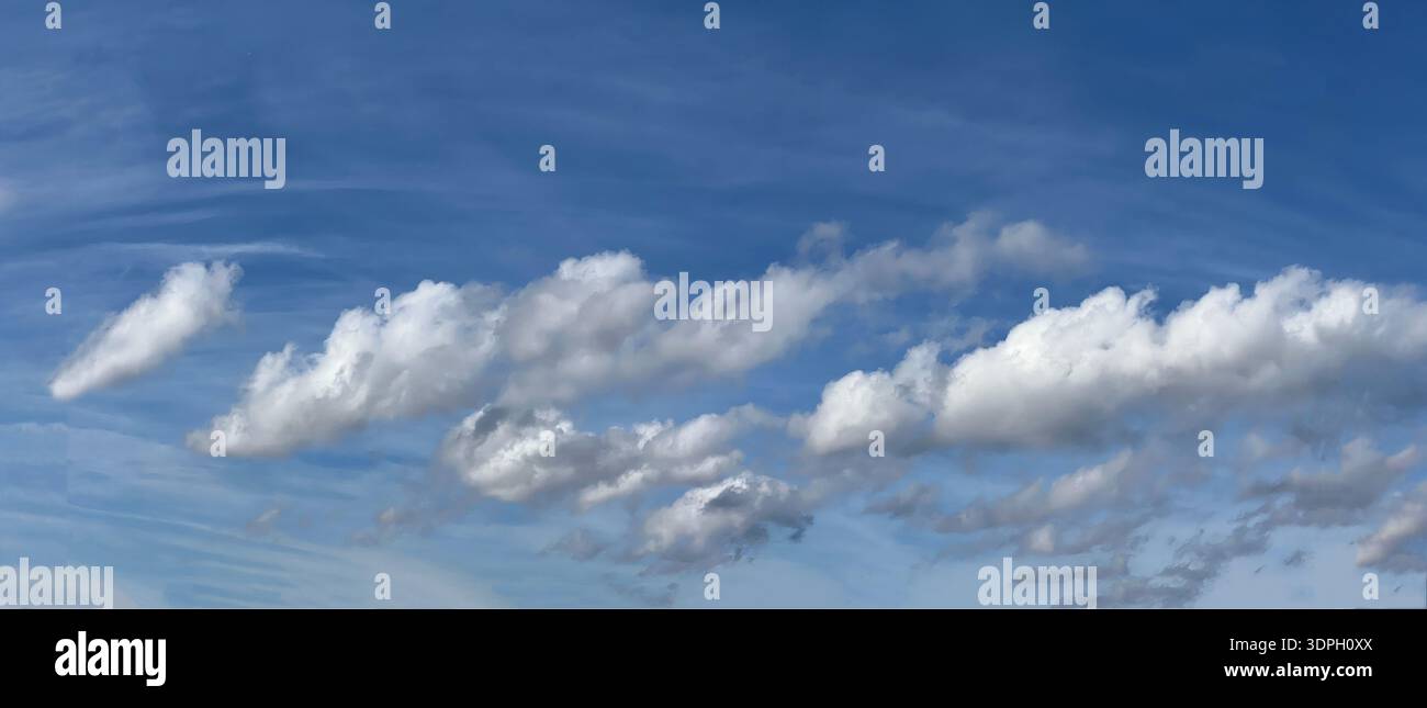 Wolken schweben an einem sonnigen Nachmittag in einem blauen Himmel. Sie wirken weich und flauschig und bewegen sich sanft über die Landschaft. Die Szene zeigt ein Gefühl der Offenheit Stockfoto