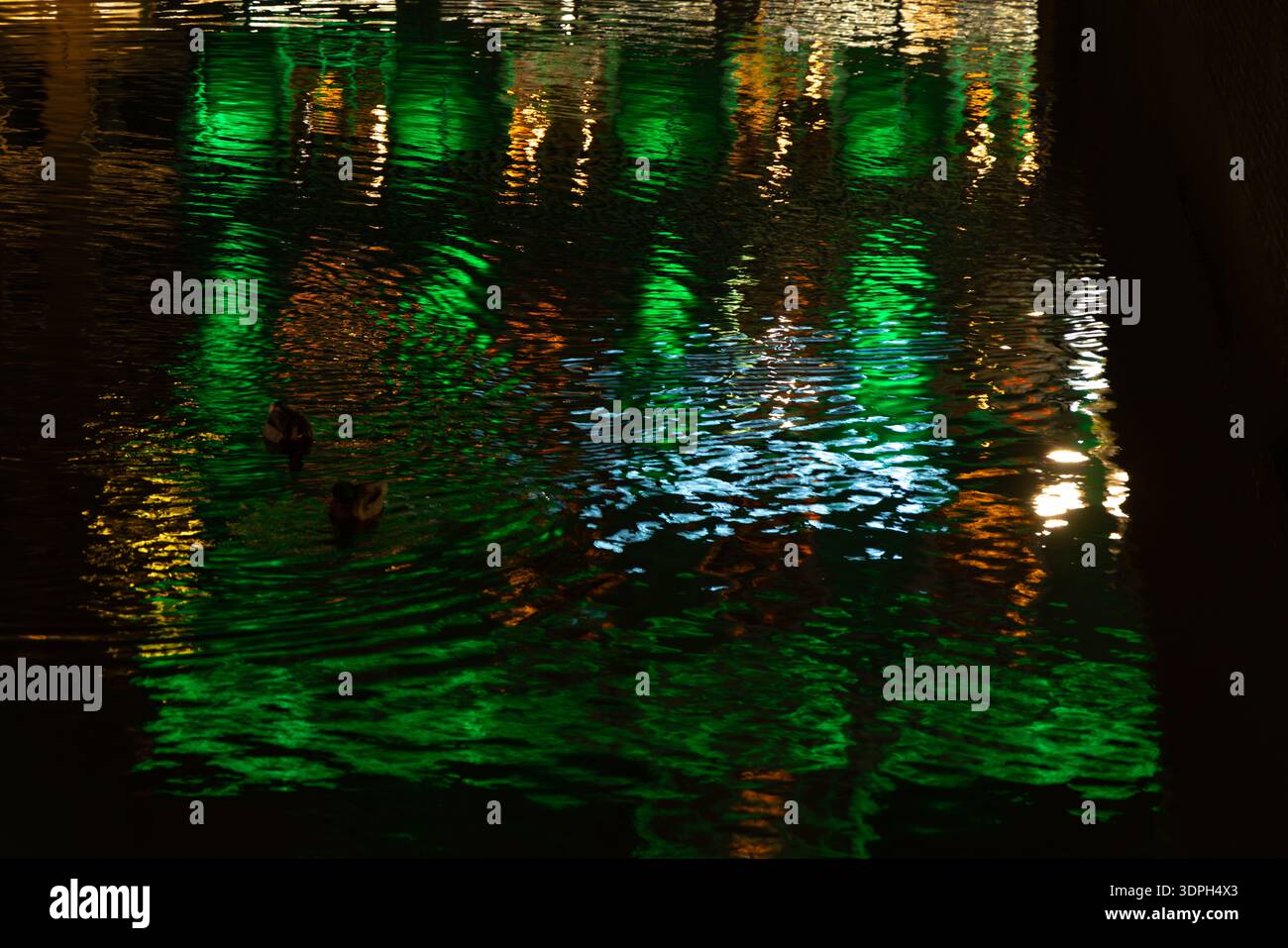 Nächtliche Stadtszene in Amsterdam, die bunte Reflexionen der städtischen Lichter auf einem Fluss zeigt, die einen wunderschönen strahlenden abstrakten und stimmungsvollen Hintergrund mit Wasserwelken und lebhaften Farbtönen schaffen Stockfoto