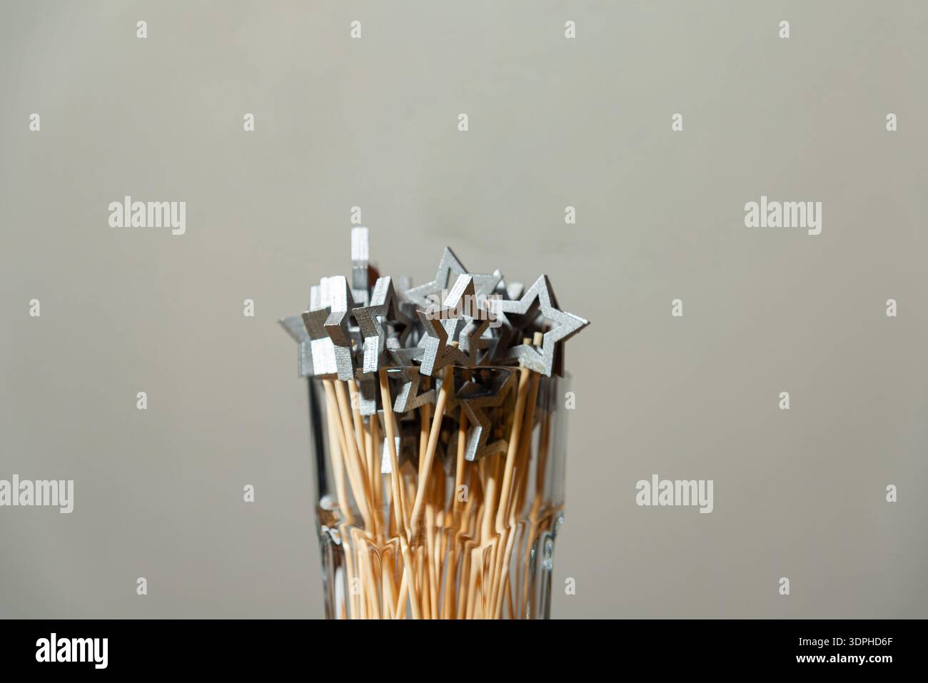 Silberne sternförmige Partyauswahl auf Holzstäben in klarem Glas, minimalistische Festdekoration auf neutralem Hintergrund mit Kopierraum. Stockfoto