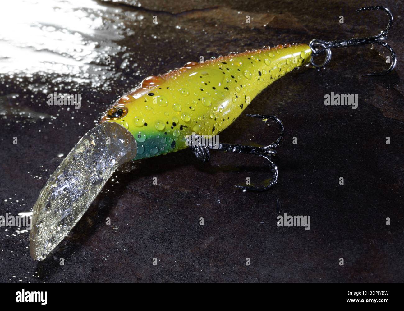 Gelber, oranger und blauer Angelköder zum Gießen mit einem großen, mit Wasser bedeckten, auf einem nassen Fels ruhenden Bann. Stockfoto