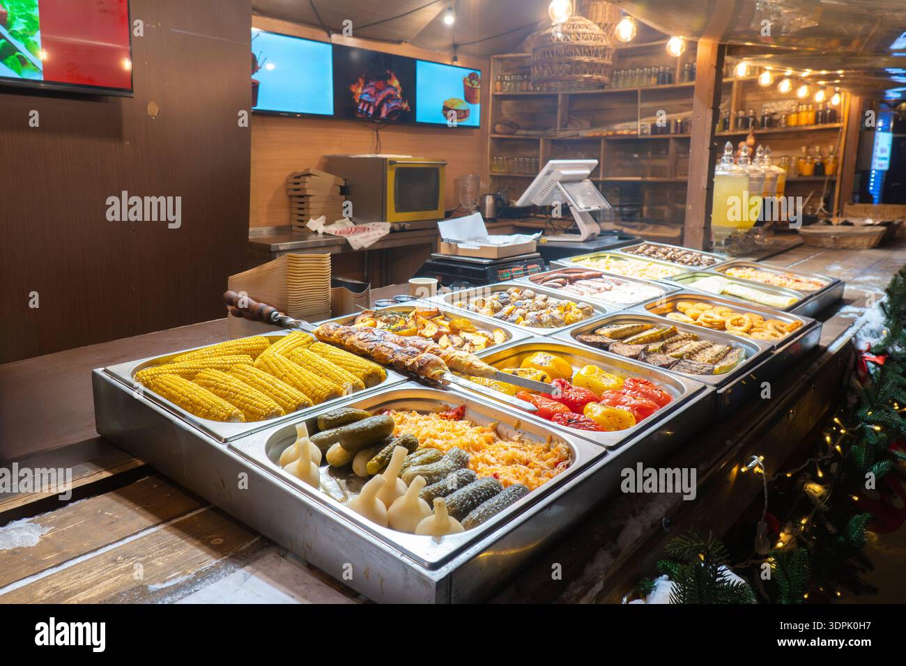 Auswahl an gegrilltem Mais, Paprika, Gurken und Knoblauch in Metallschalen an einem Imbissstand im Freien. Köstliche vegetarische Catering-Optionen Stockfoto