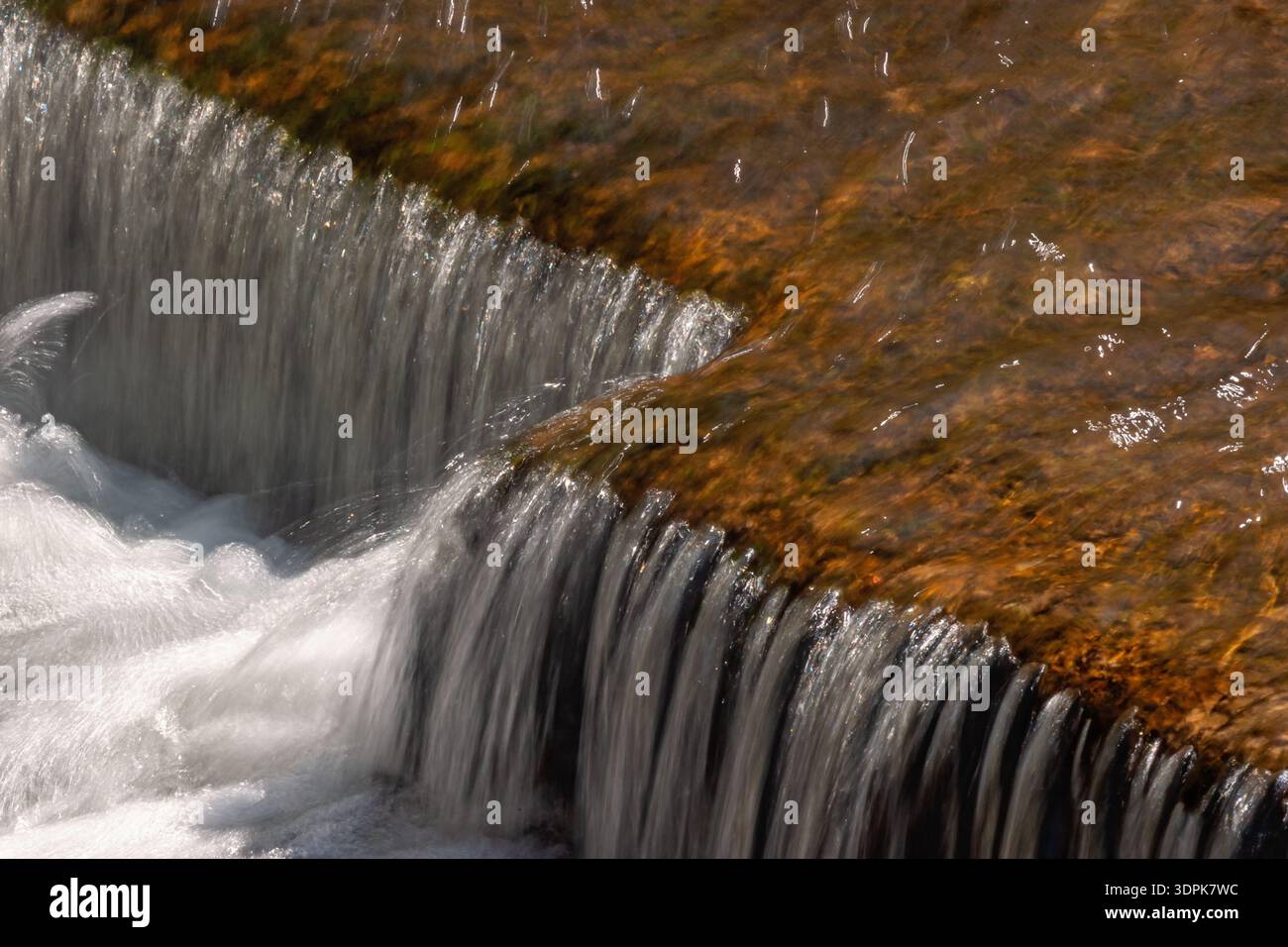 Kleiner Wasserfall über einem Felsen mit goldbraunem Wasser Stockfoto