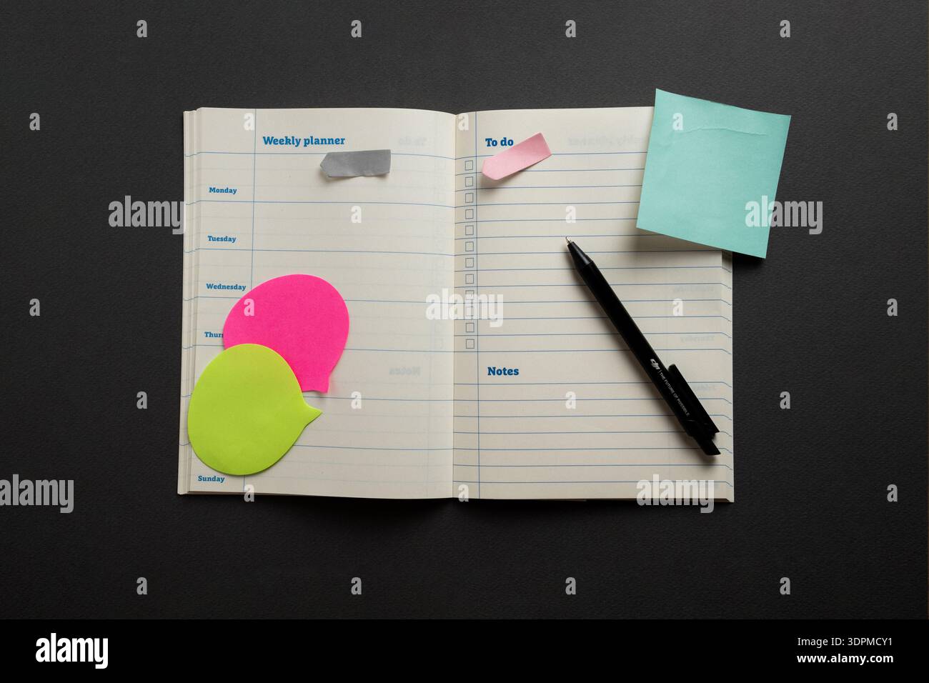 Öffnen Sie den Wochenplaner mit farbenfrohen Haftnotizen und Stift auf dunklem Hintergrund, minimalistischem Planungs- und Organisationsarbeitsbereich. Stockfoto