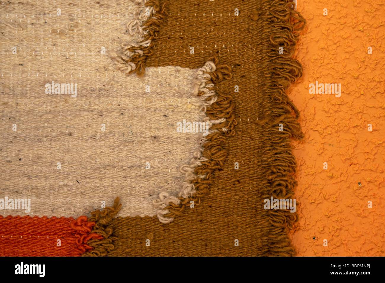 Nahaufnahme der Textur eines handgewebten Teppichs. Strukturierter Hintergrund mit warmen Erdtönen. Feinmotorik, Waldorfpädagogik, Rudolf Steiner, ganzheitlich e Stockfoto